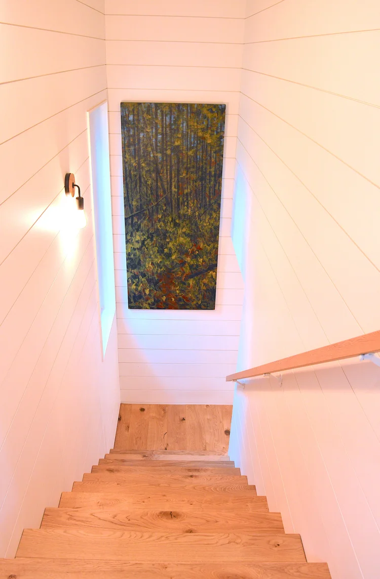 Modern two-story home with large glass windows, warmly lit interiors, and a balcony. Surrounded by trees and a manicured lawn at dusk. Cozy ambiance.