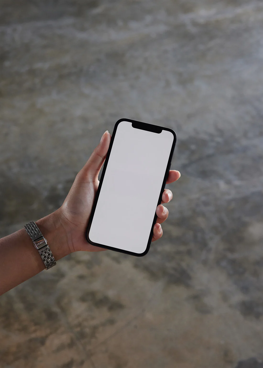 A hand holding a black iPhone displaying a minimalist website interface with a focus on night photography. The background features a textured concrete floor, creating a clean, modern aesthetic.