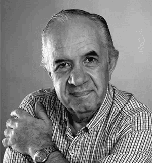 Smiling blonde woman with freckles in a white shirt, arms crossed, minimalist studio portrait.