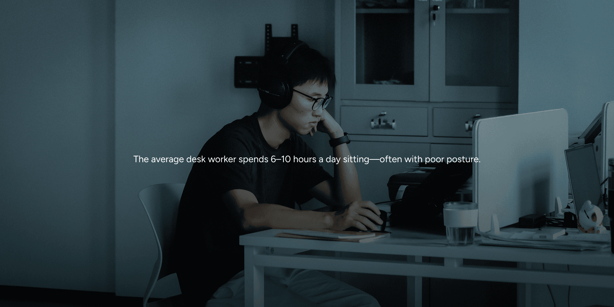 Man at desk with headphones, hunched over.