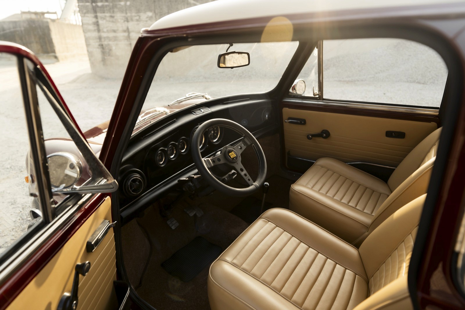 Interior of a vintage car featuring a wooden dashboard and light-colored leather seats. Bright lighting enhances details.