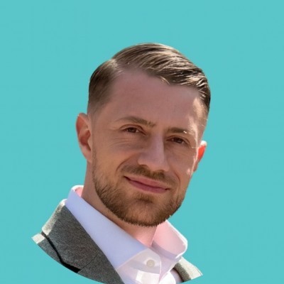 A smiling person with short, dark hair and a light-colored shirt against a dark background.