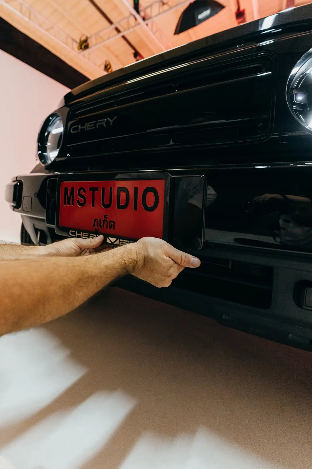 Fitting an MStudio plate on the glossy black front of the Chery V23, with studio lights reflected in the paint