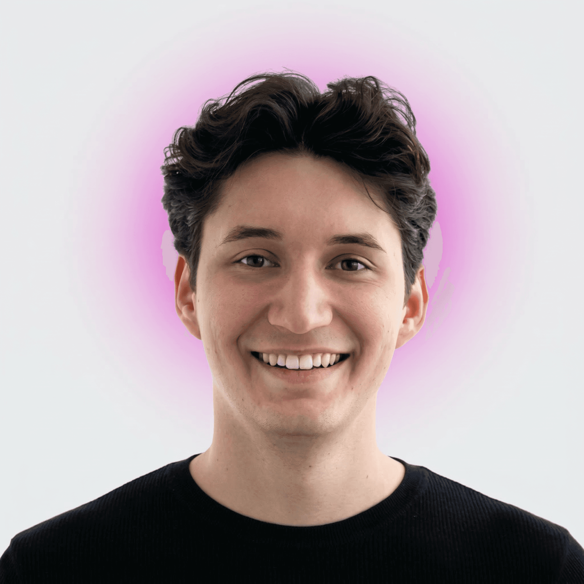 Smiling young man with curly hair, wearing a dark hoodie, against a softly lit background.