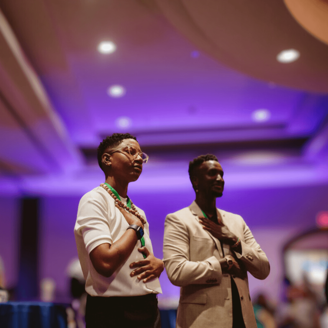 Two individuals stand side by side, dressed formally, in a venue with purple lighting.