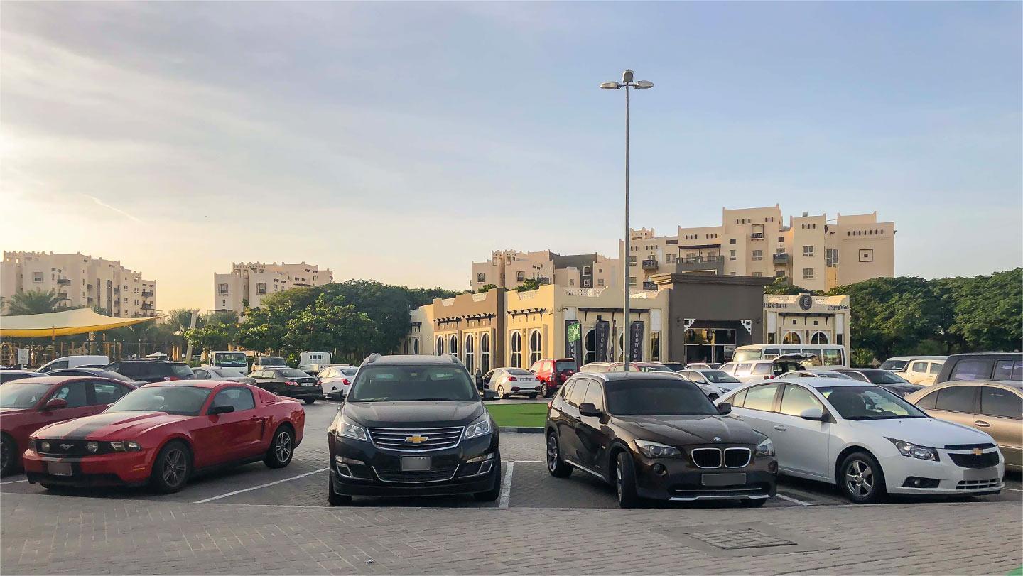 Cars parked in Remraam Dubai near beige buildings with Middle Eastern design and palm trees under a clear sky.