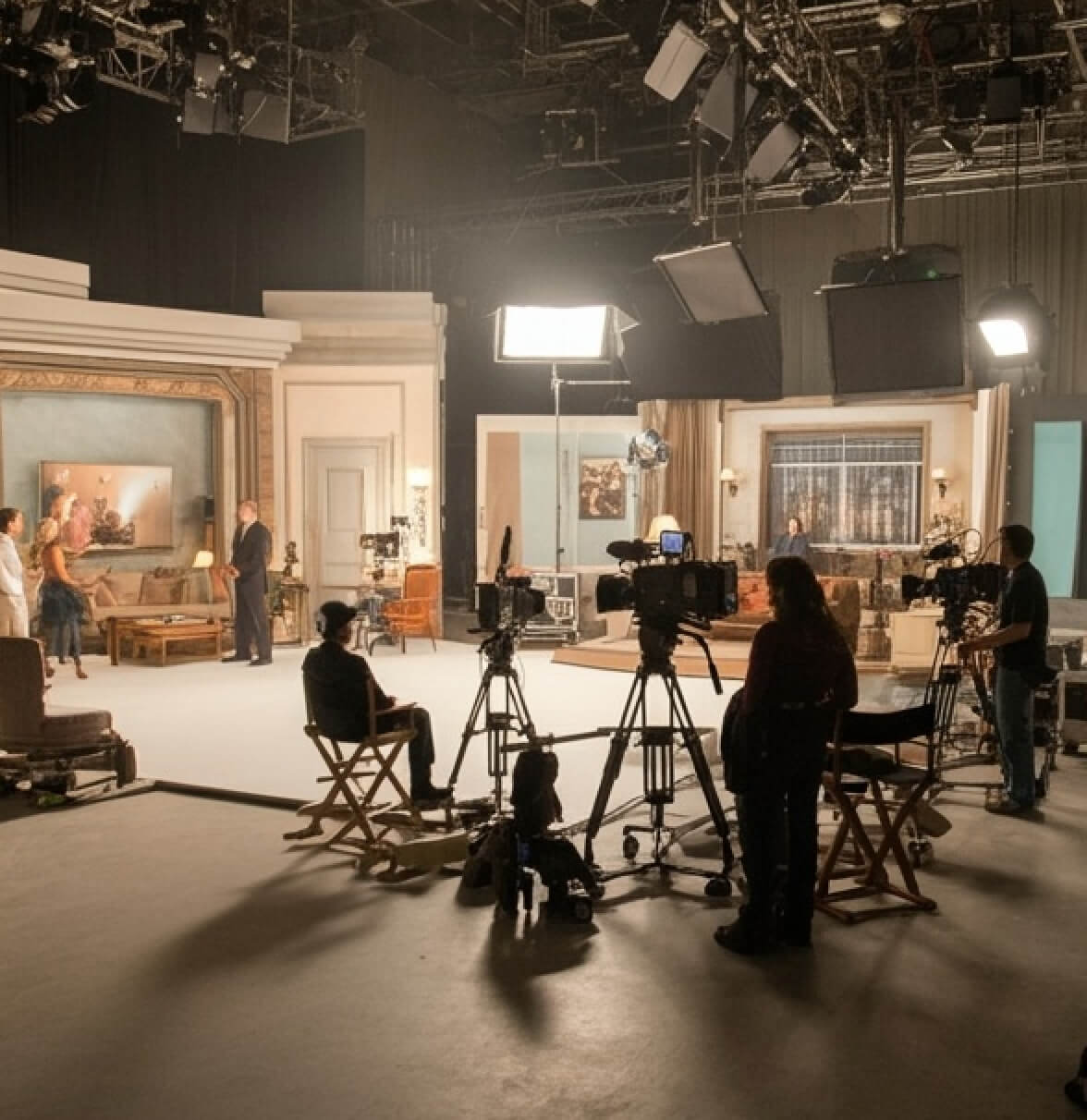 A film set with cameras, crew members, and lighting equipment ready for a shoot in a well-lit studio space.
