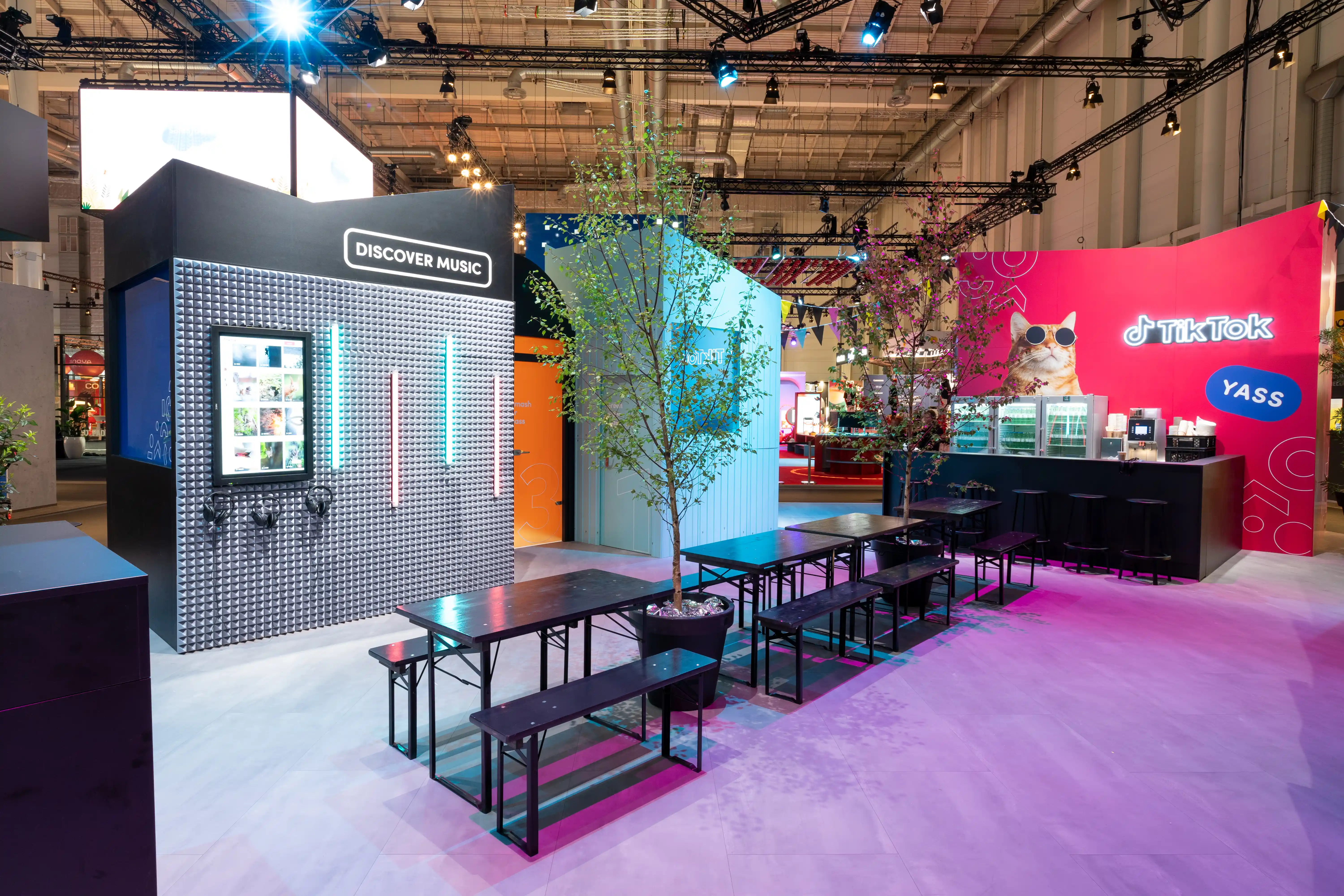 Seating area with black beer benches and trees between the Discover Music box and the red TikTok bar at OMR.