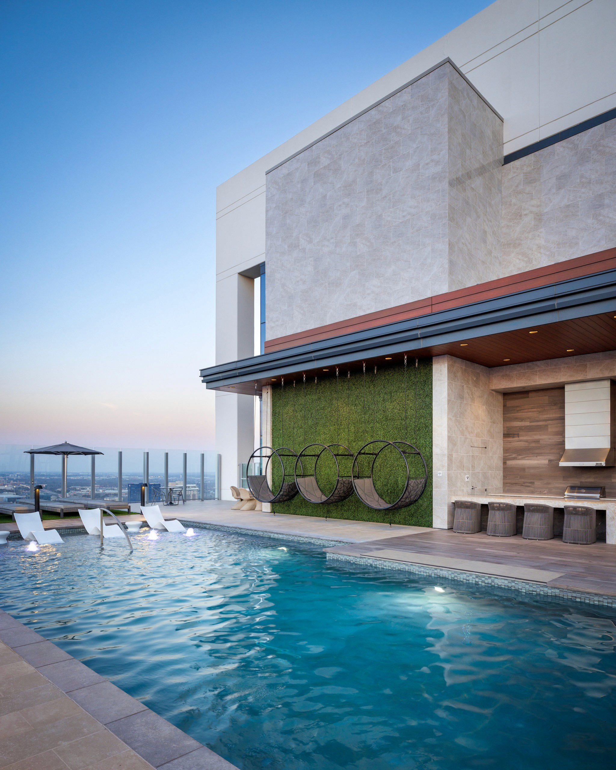 Rooftop pool with lounge chairs, hanging swings, and outdoor kitchen.
