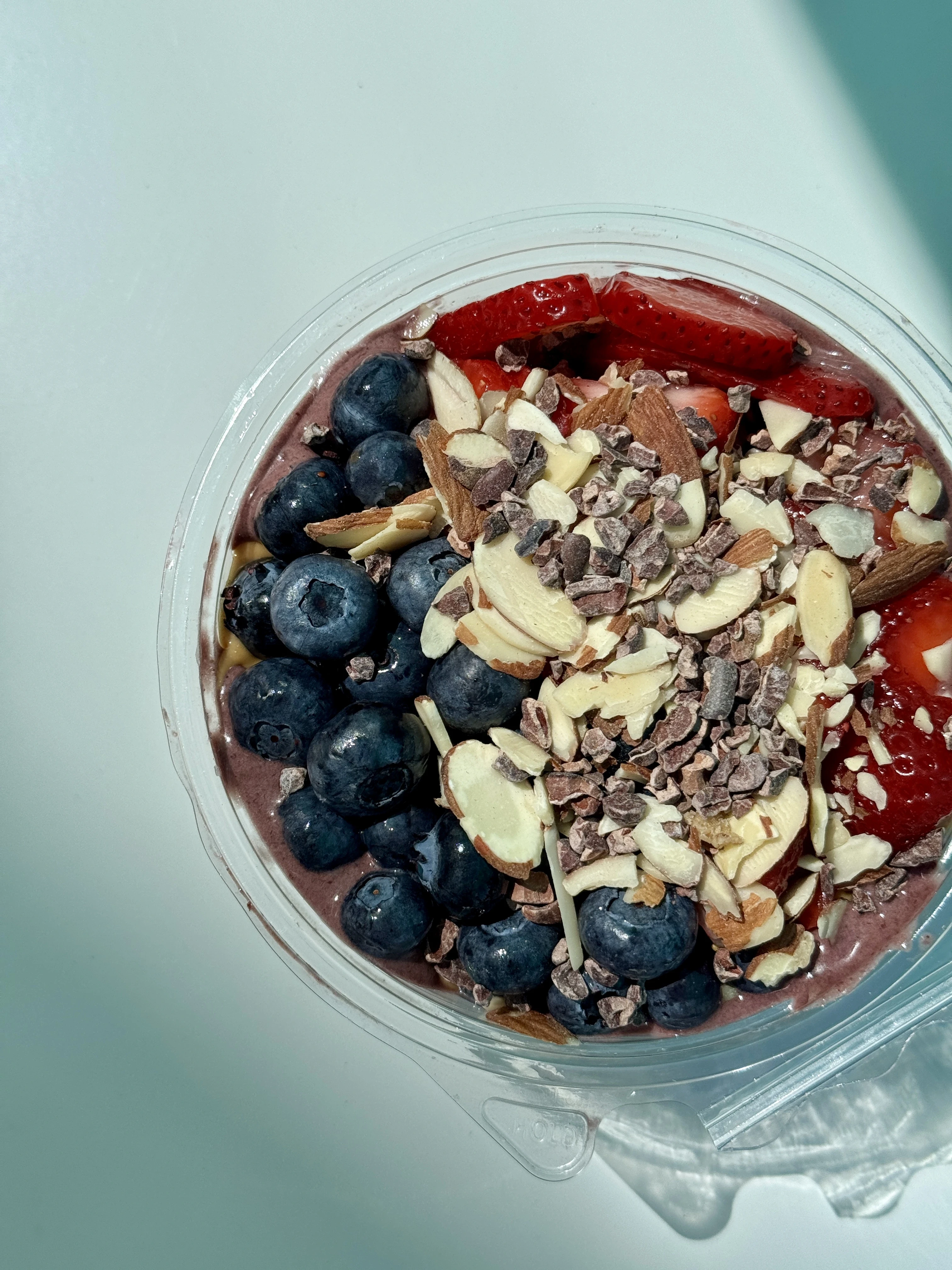 acai bowl with blueberries, sliced almonds, cacao nibs, sliced strawberries and a drizzle of peanut butter