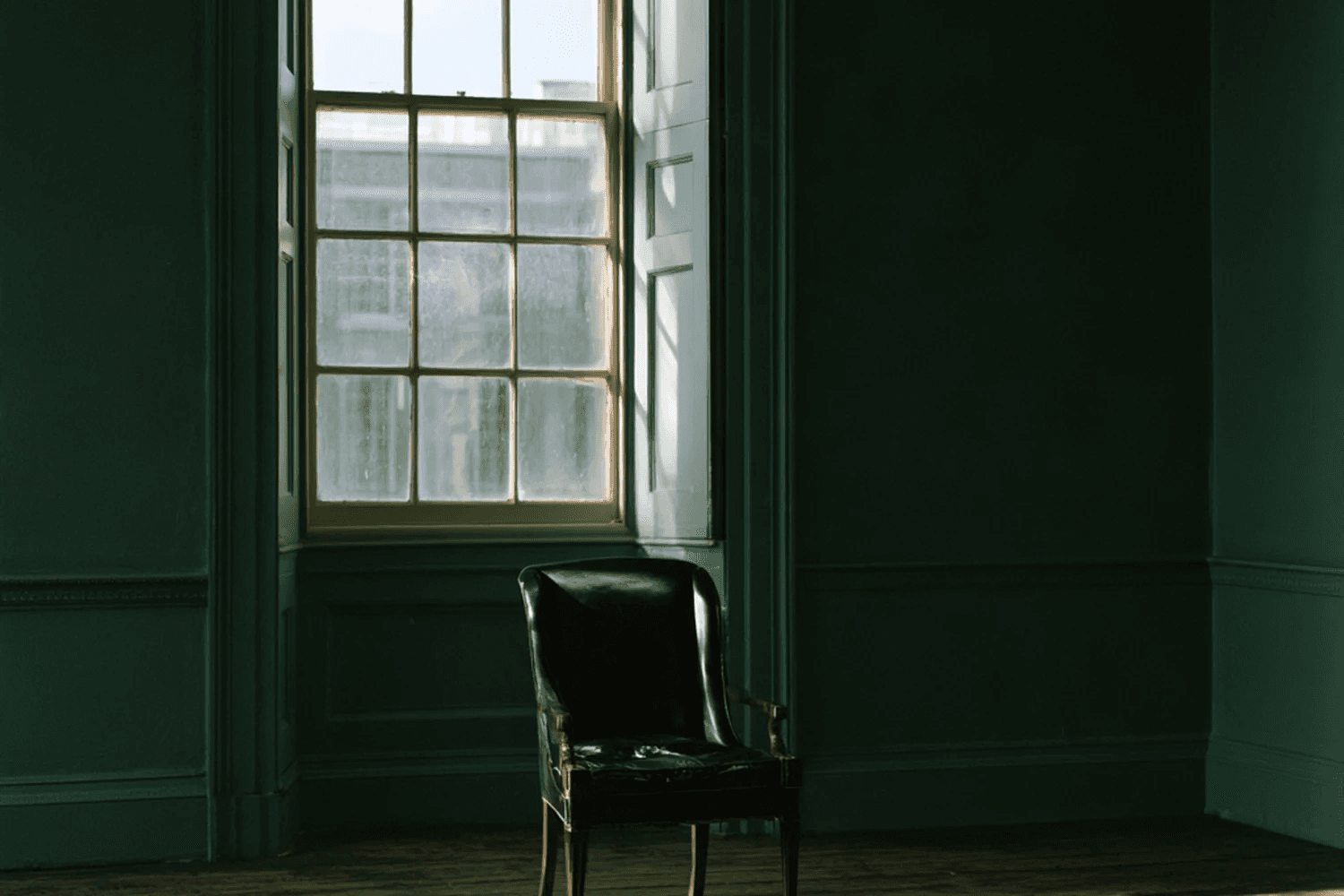 Dark green room with a tall window and a leather chair
