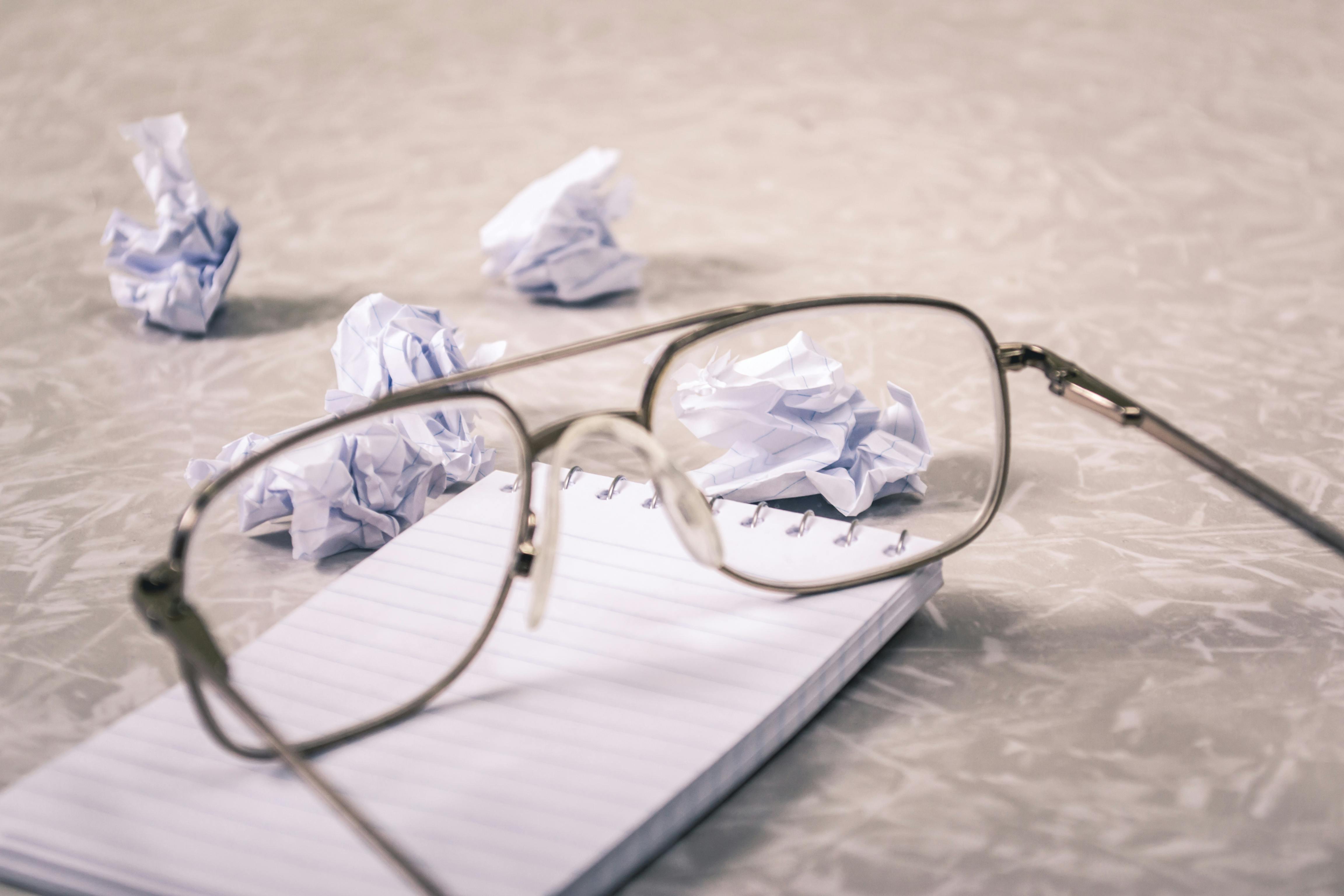An eyewear placed on top of a notebook with scattered pieces of torn papers