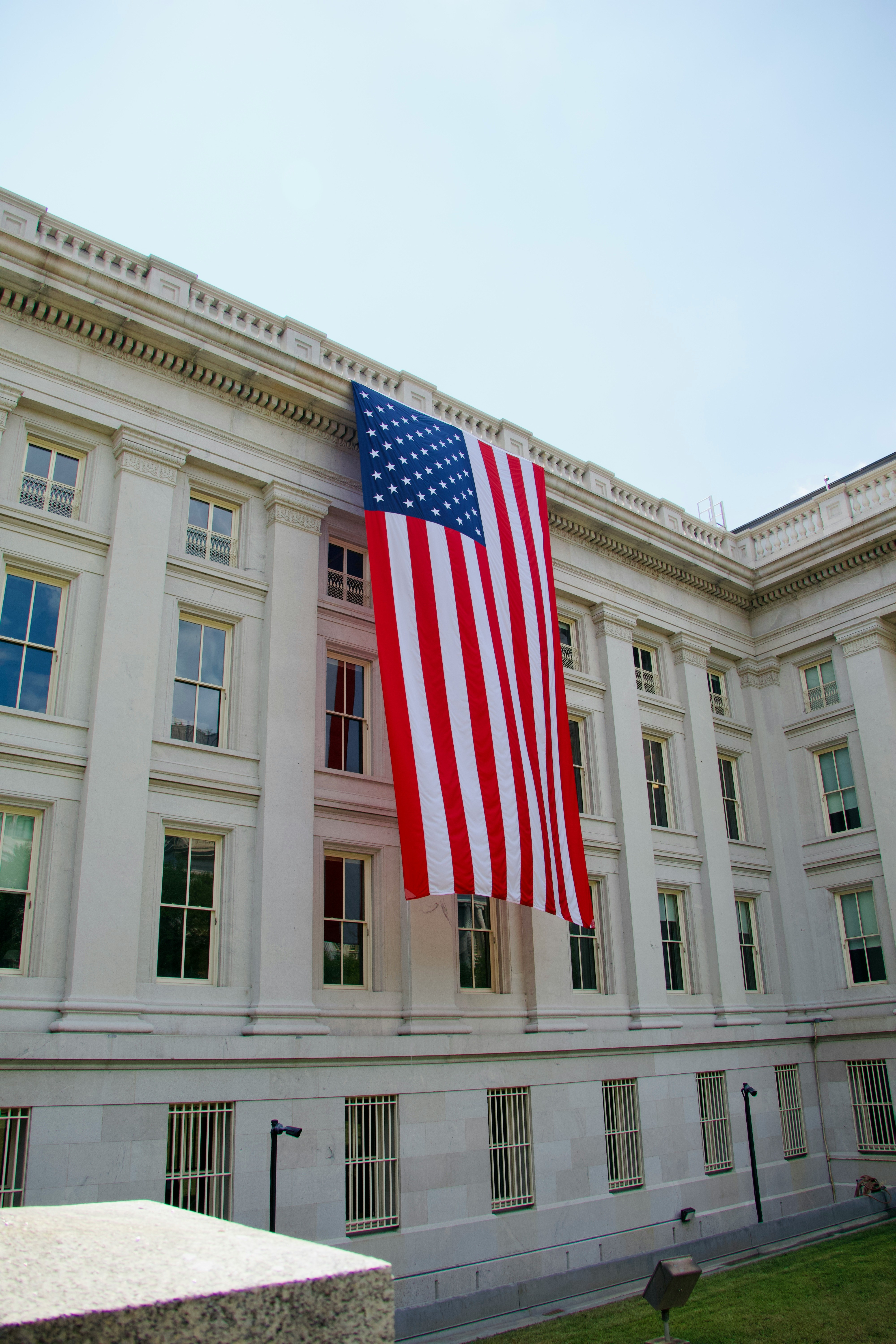 Large american flag hangs from a white building.