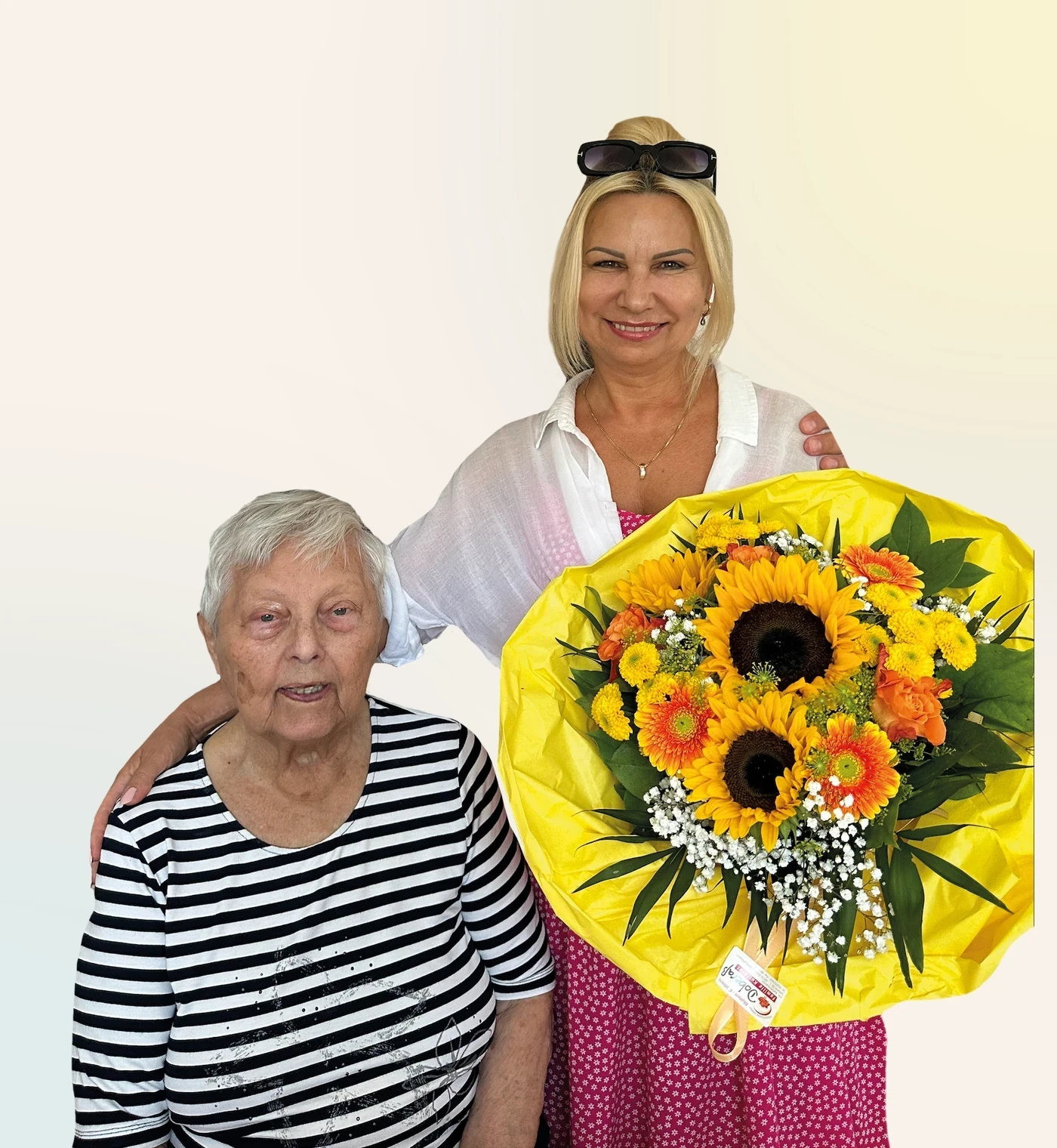 Eine ältere Frau und ihre Begleiterin halten einen großen Sonnenblumenstrauß.