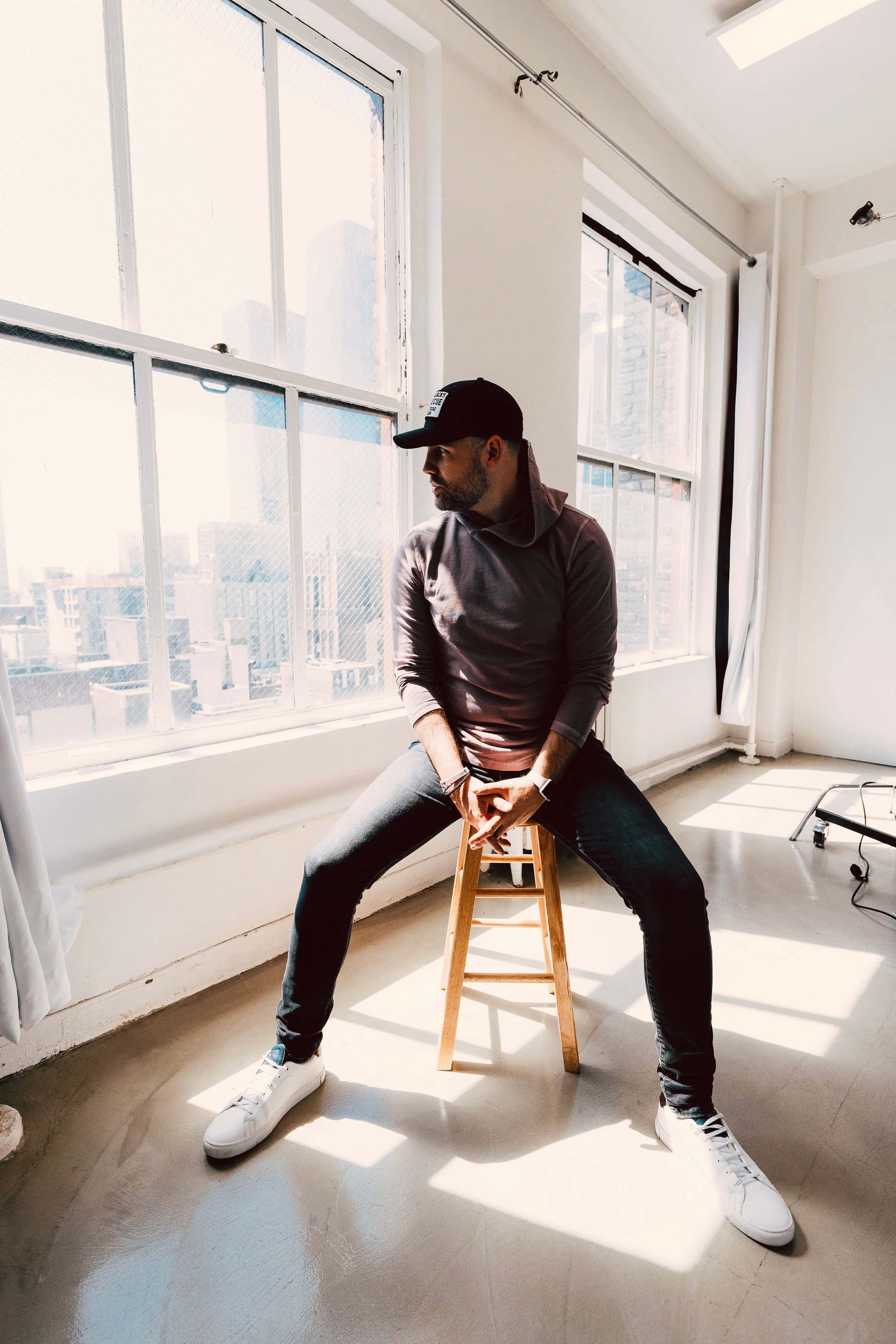 Designer Chadd Weston sitting on a stool looking out the window during a photo shoot on Manhattan