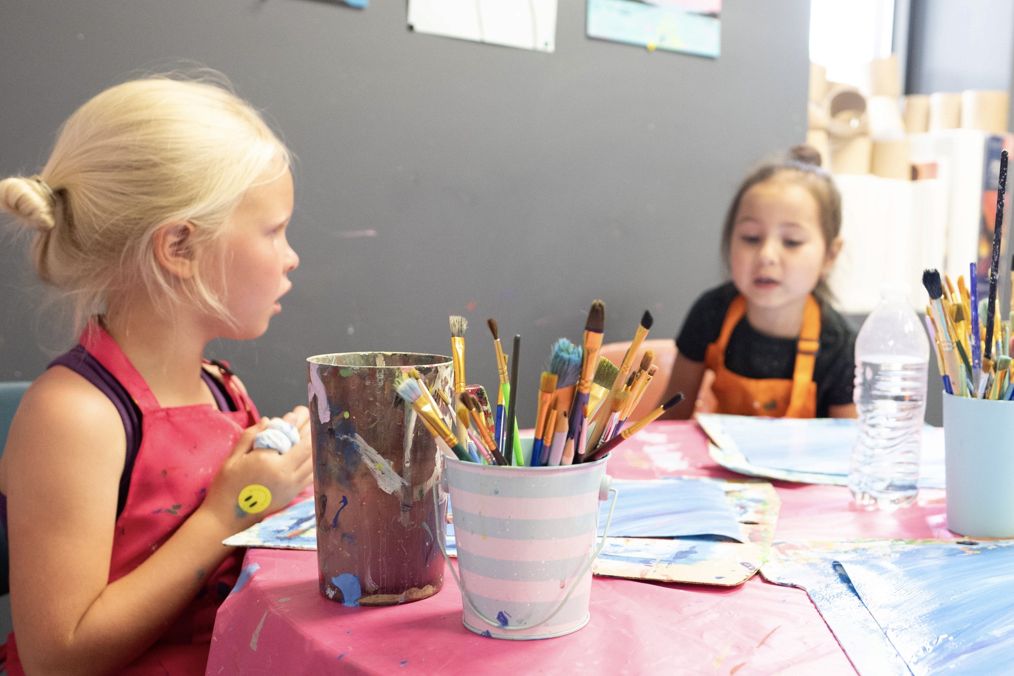 Two young girls at art class sitting at a pink table painting