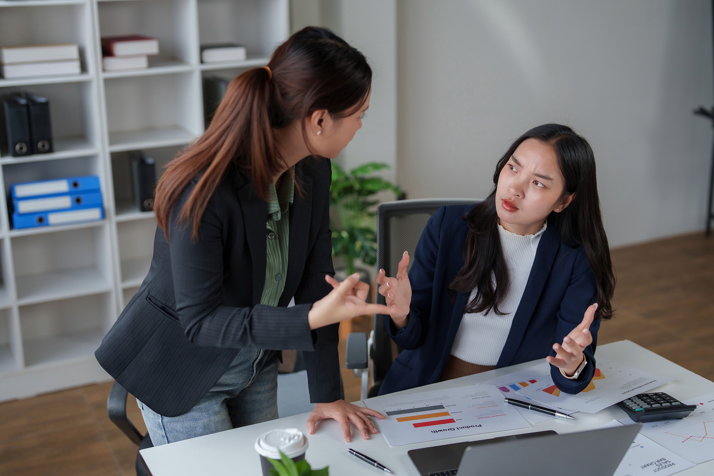 Two asian businesswomen in office discussing an argument, problem, or conflict at work. They are having a serious, tense conversation