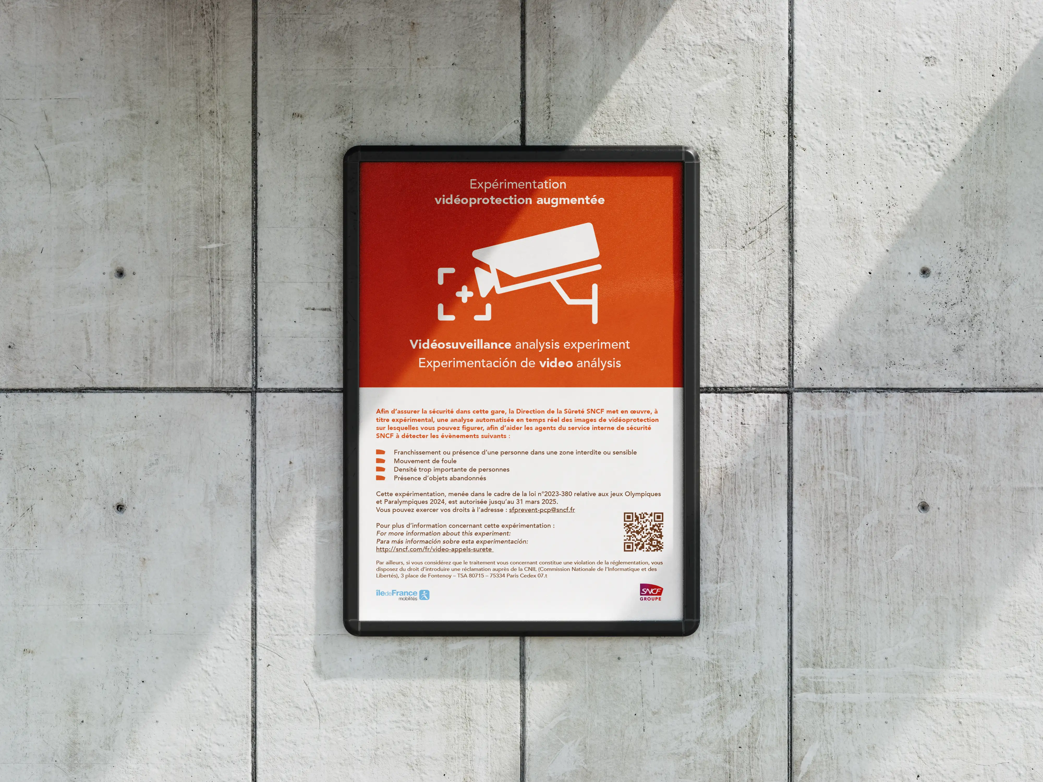 Framed RATP and SNCF information poster mounted on a concrete wall, featuring an orange surveillance camera pictogram and multilingual text about enhanced video monitoring.