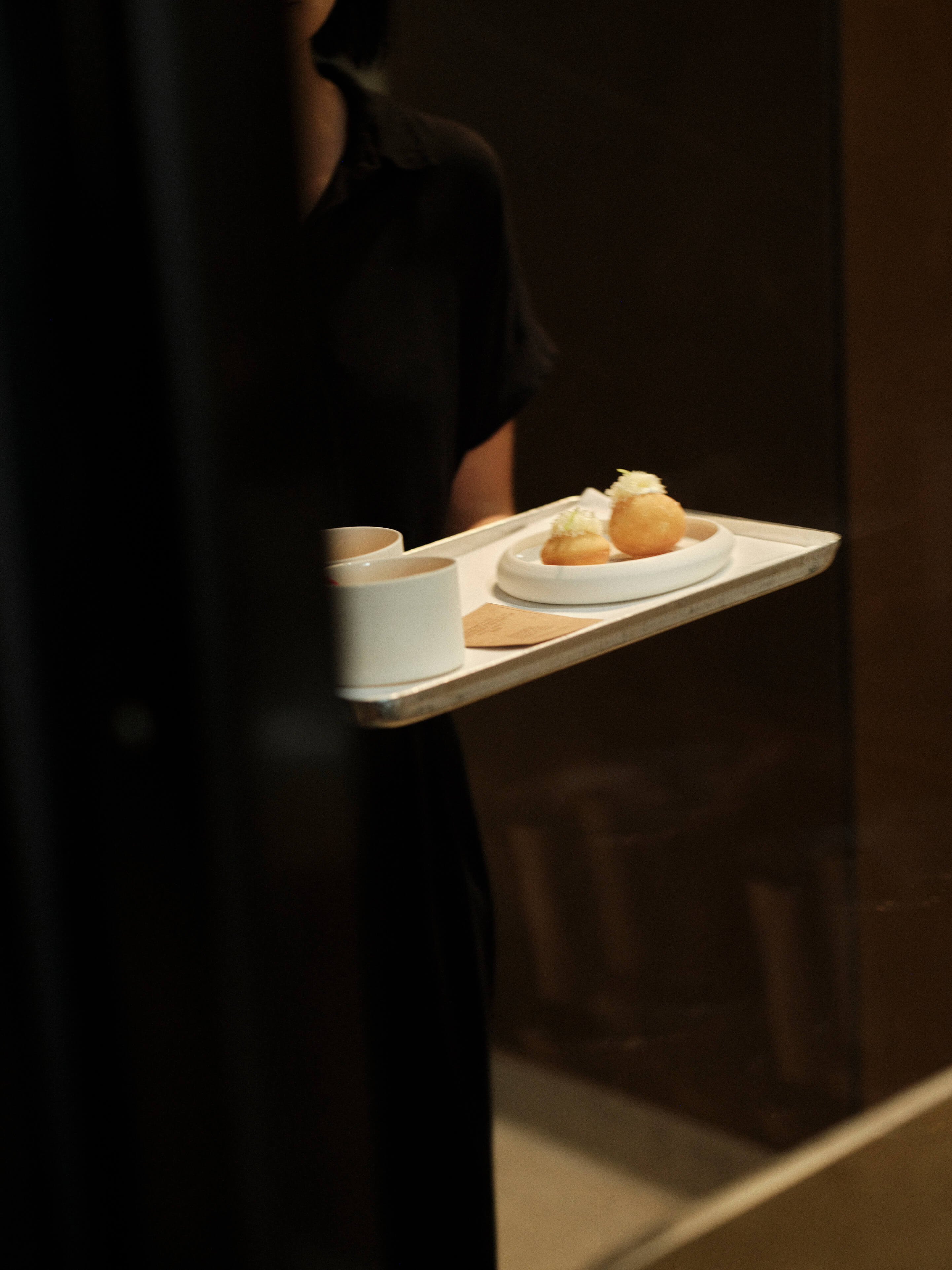 The server is carrying a tray with small hors d'oeuvres on a plate in a restaurant setting.