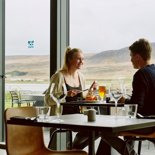 Two people dine at a restaurant, sitting by large windows with a scenic view of a mountainous landscape.