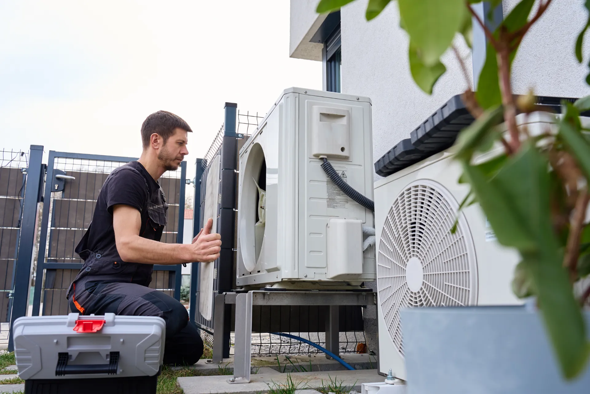 Ein Handwerker, welcher gerade eine Wärmepumpe vorne öffnet.