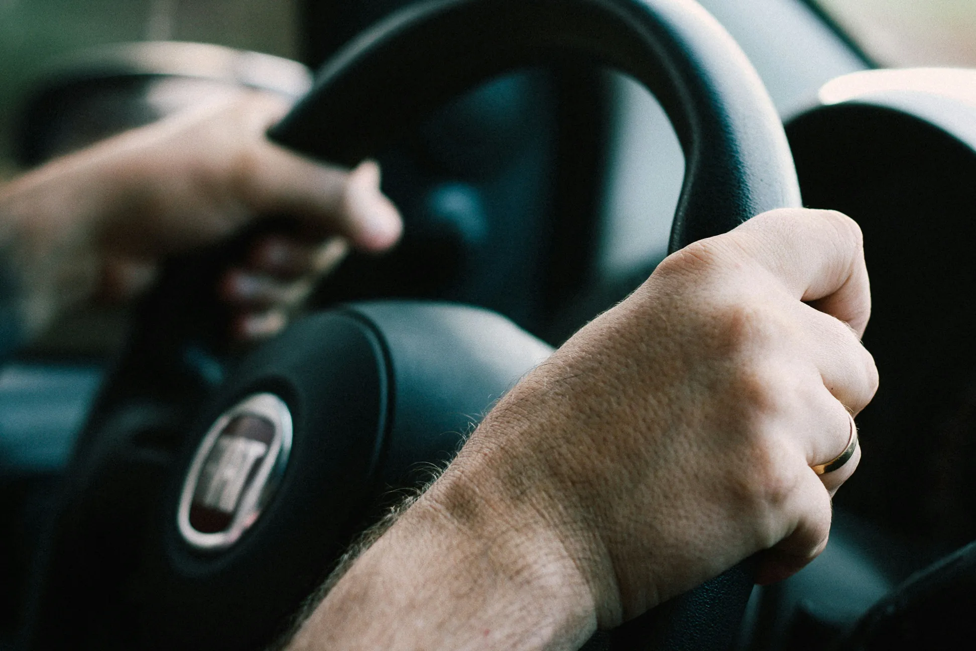 Nahaufnahme von zwei Händen am griffigen Lederlenkrad eines Fiat-Fahrzeugs während einer praktischen Fahrstunde.