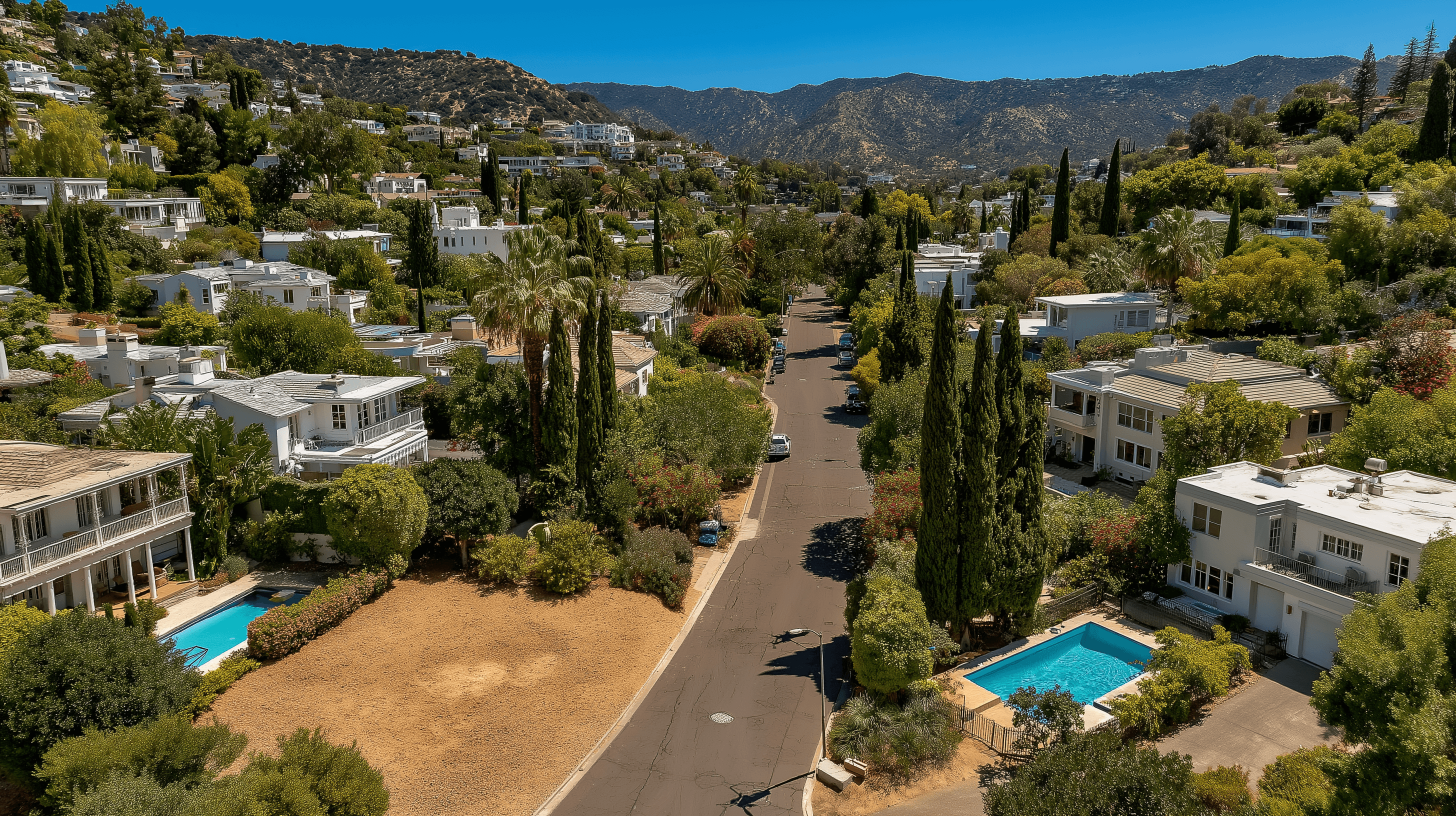 Elevated street-level view of a lush suburban neighborhood featuring white luxury homes with private pools, tall cypress trees, and mountains in the background.