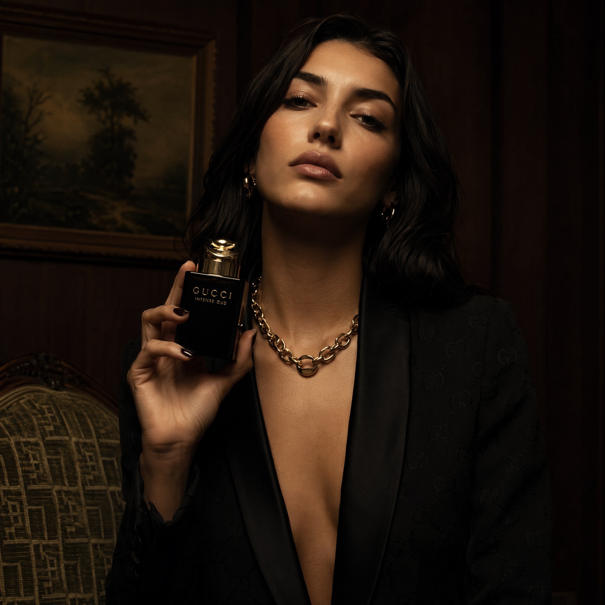 25 year old brunette woman, sat in a dark luxury room holding perfume