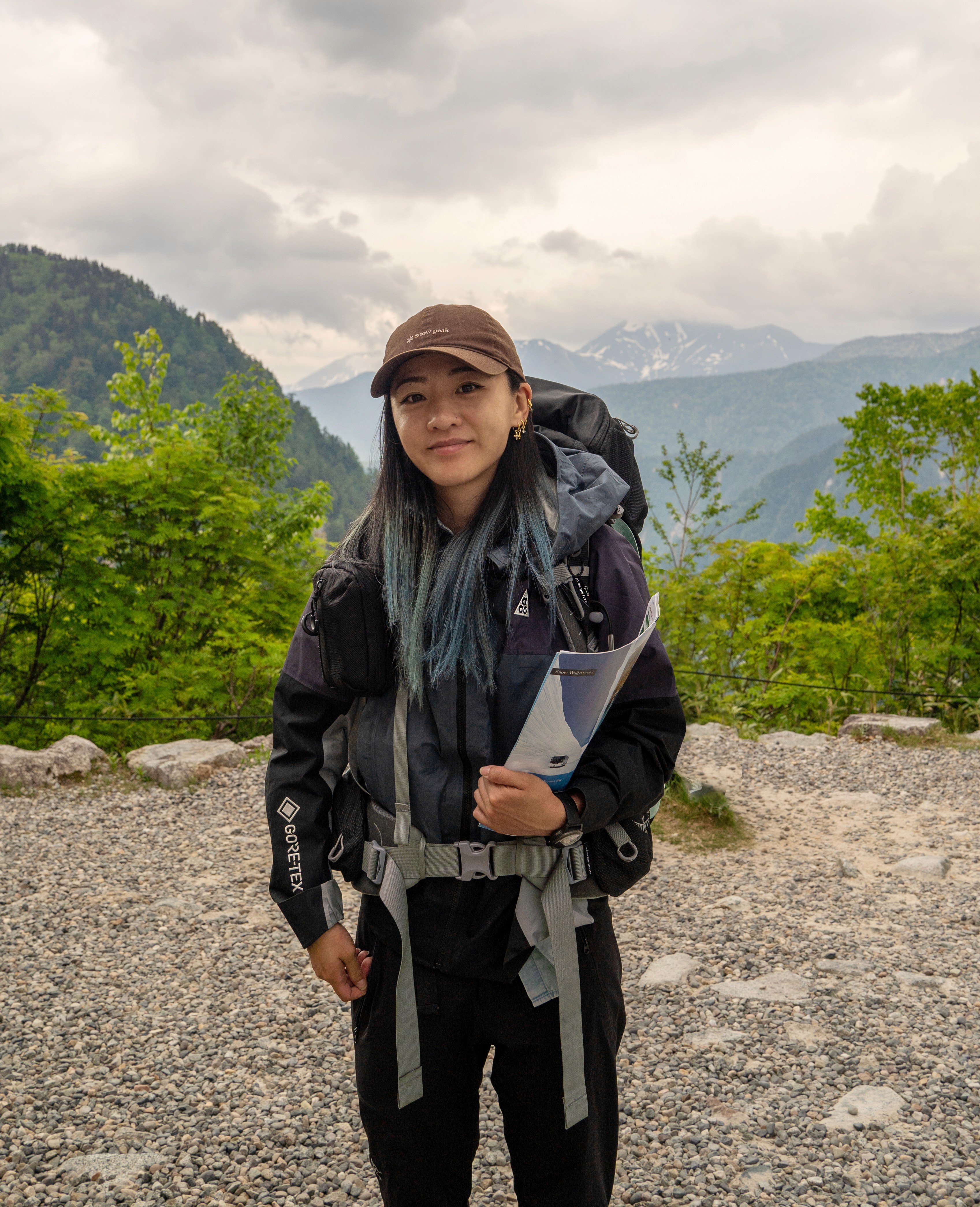 A young person with long, wavy hair sits in front of a plain background, looking directly at the camera.