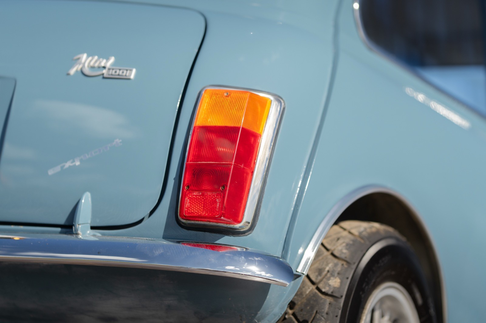 Close-up of a light blue car's rear, showing the red and orange tail light and part of the rear bumper.