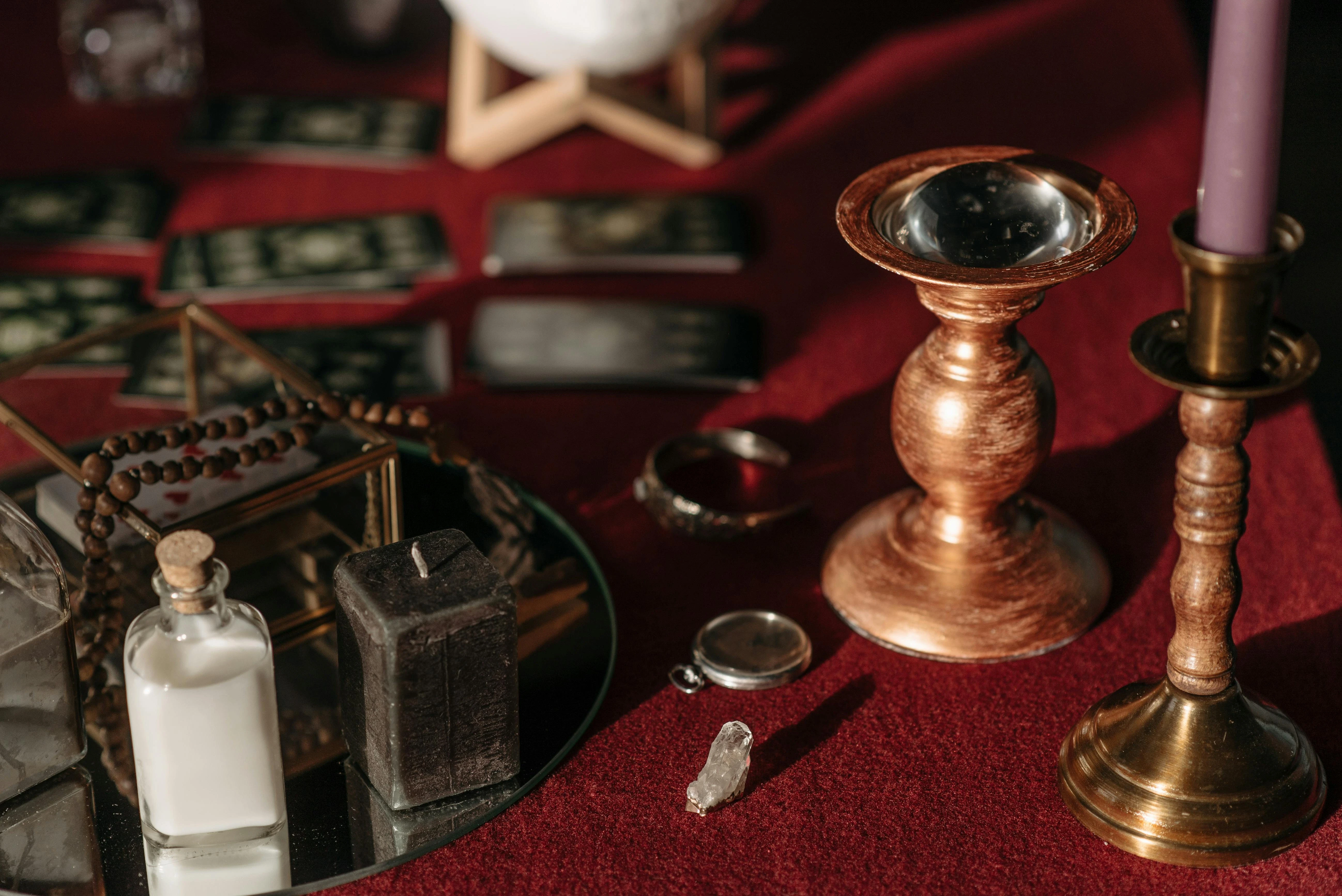 A mystical tarot reading altar featuring a crystal on a brass stand, a black candle, and ritual tools spread across a deep red velvet cloth.