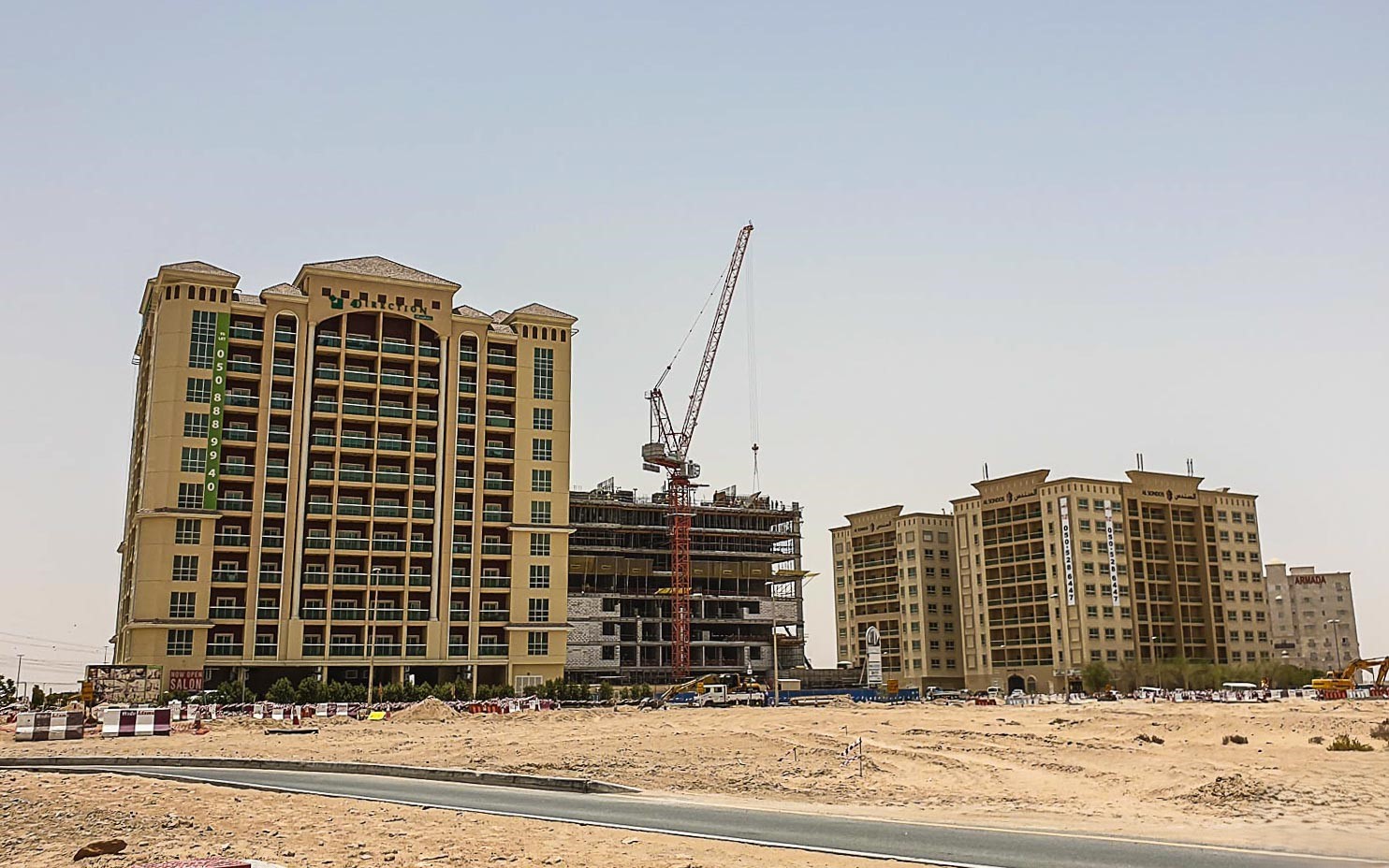 Modern residential buildings at sunset with glowing lights and palm trees in Dubailand Residence Complex.