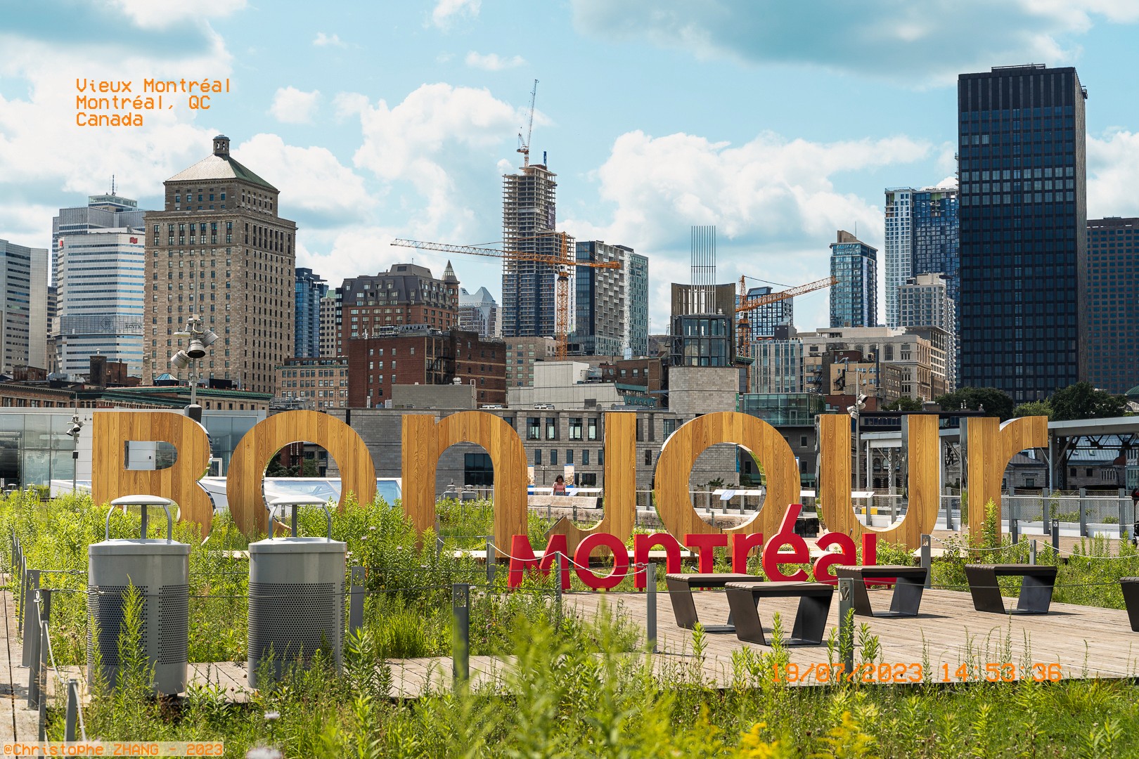 Enseigne “Bonjour Montréal” au milieu de verdure, avec le centre-ville en arrière-plan.