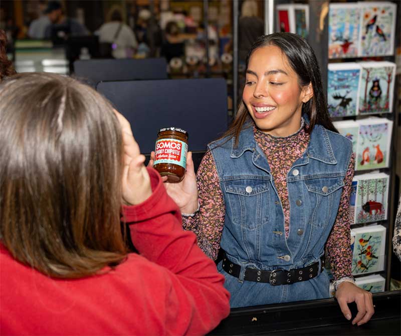 Ayde shows her Somos Smoky Chipotle salsa to the cashier.