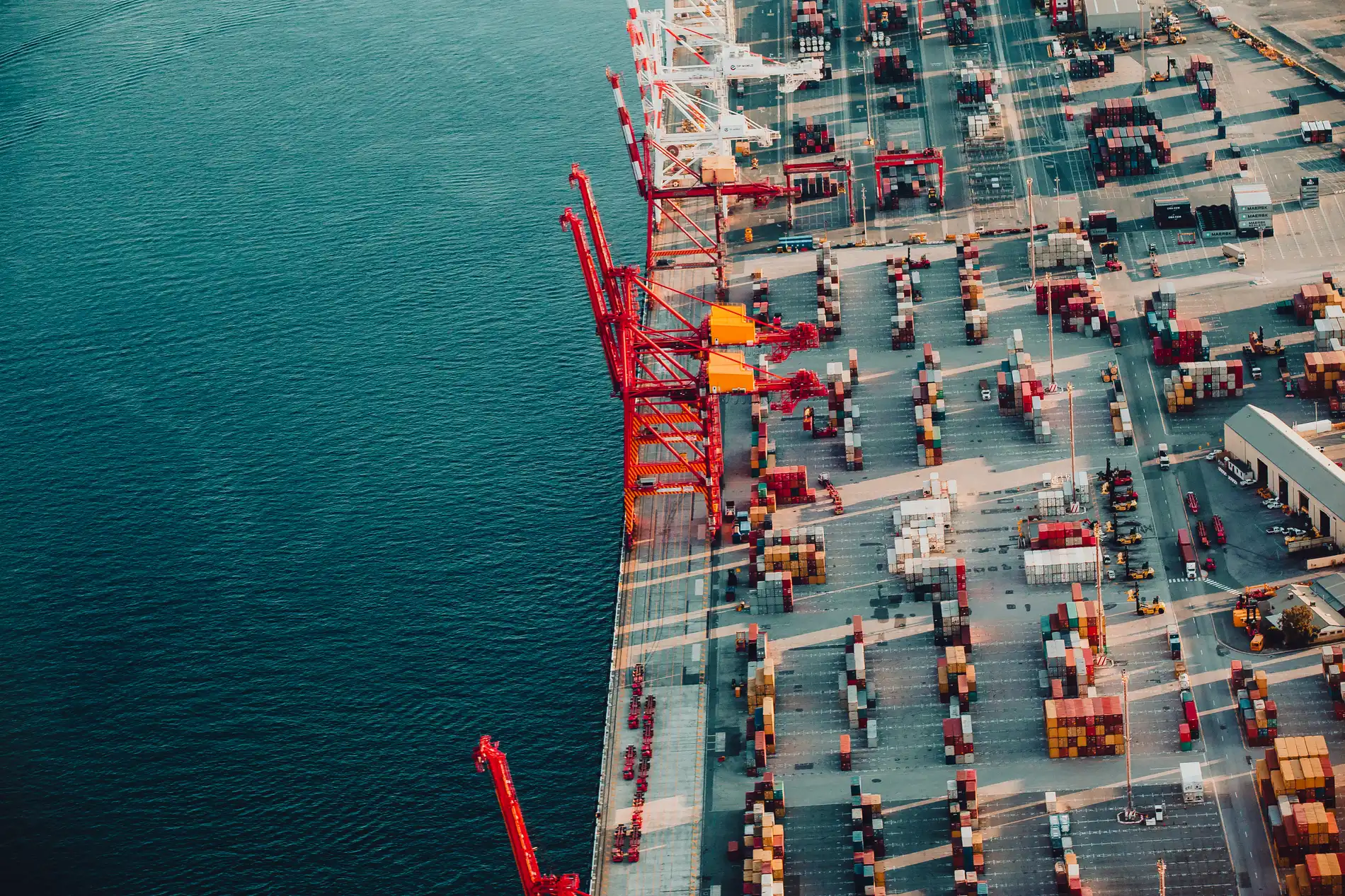 Close aerial of red gantry cranes and rows of shipping containers on a working wharf