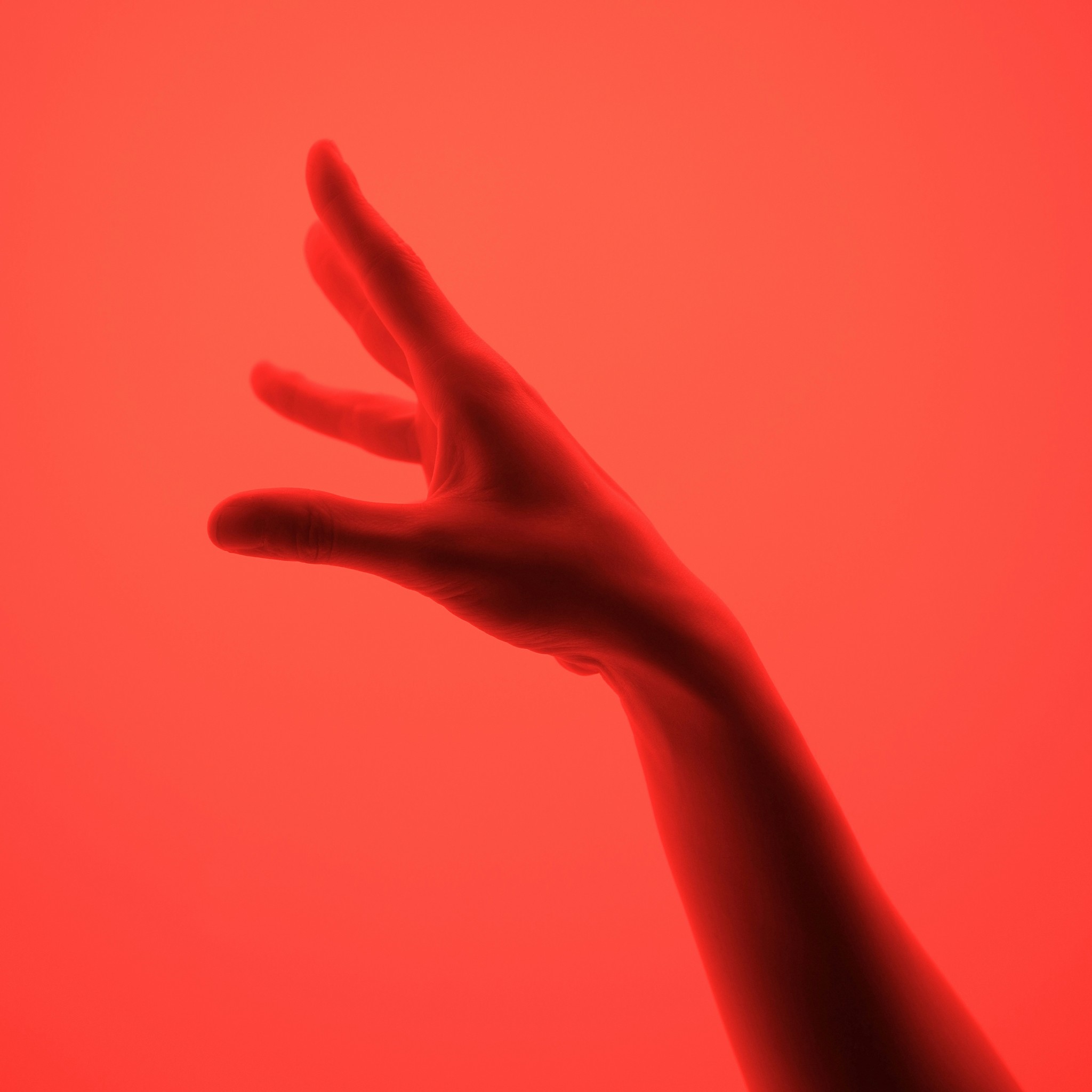 Silhouetted human hand reaching out gracefully on a bold red background, symbolizing connection, creativity, and expression. The minimalistic design and soft lighting evoke a sense of emotion, movement, and mystery, making it ideal for artistic, conceptual, or abstract themes.