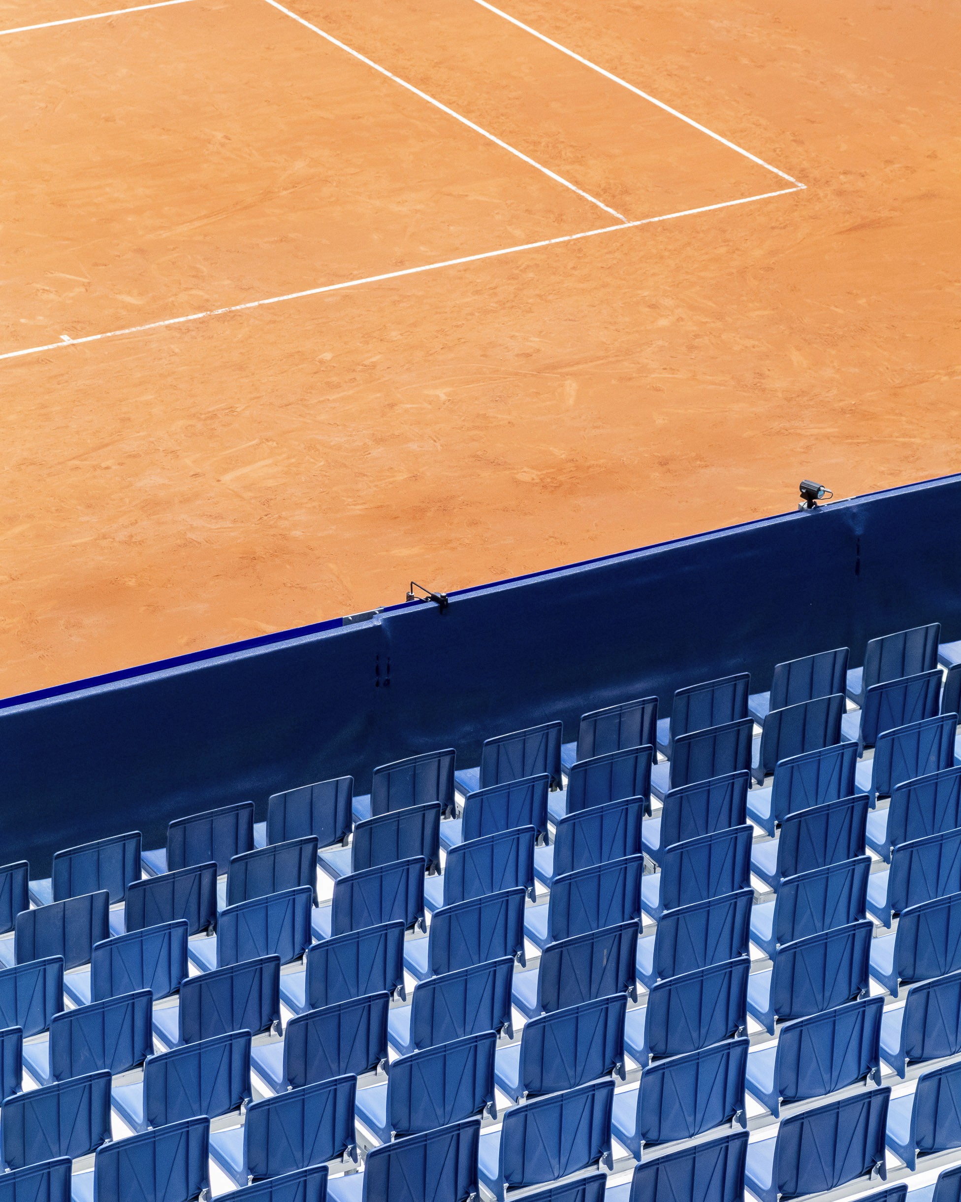 Détail d'un court de tennis avec les gradins bleus en premier plan qui sont vides