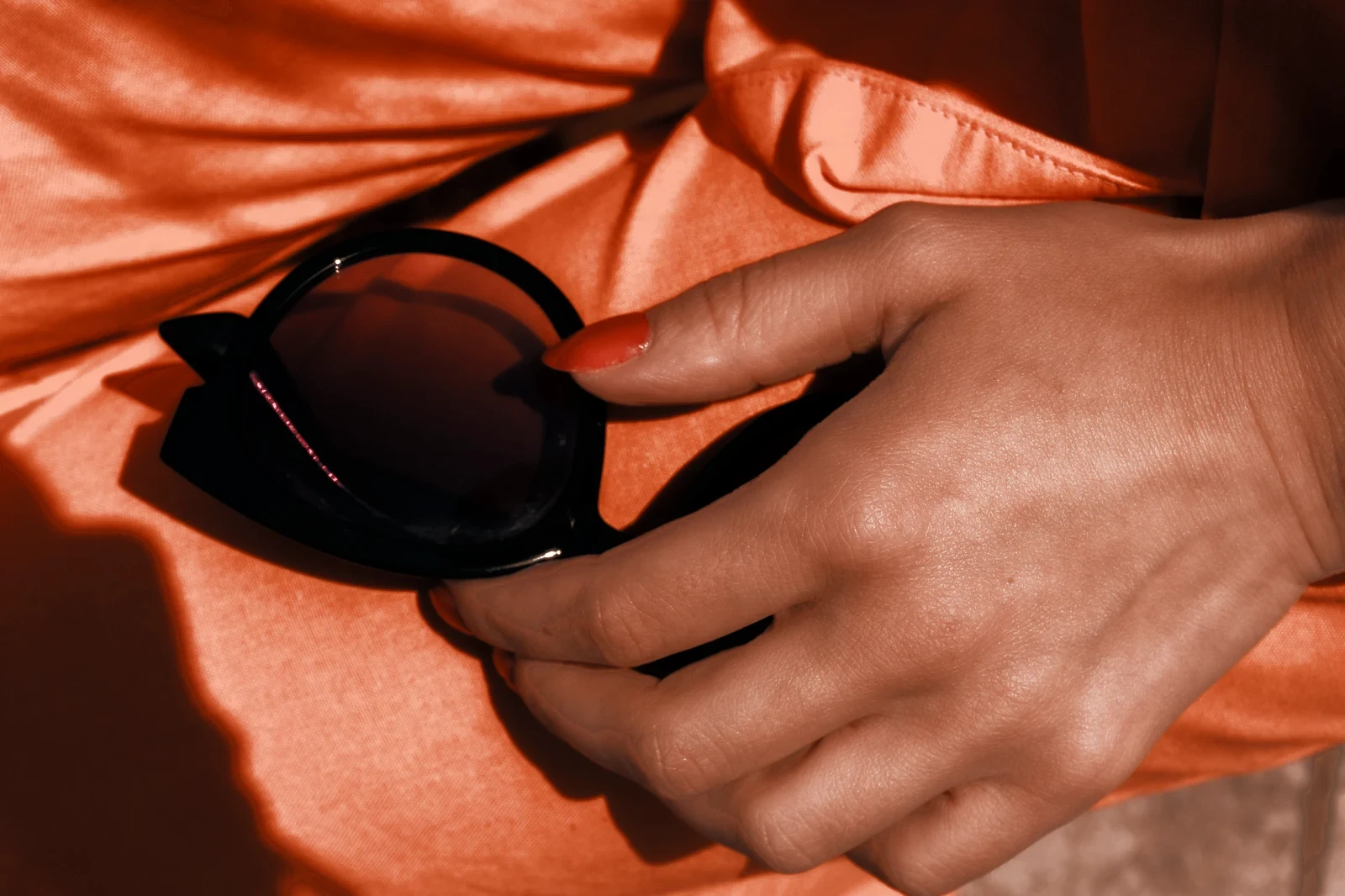 A hand holding sunglasses on orange fabric