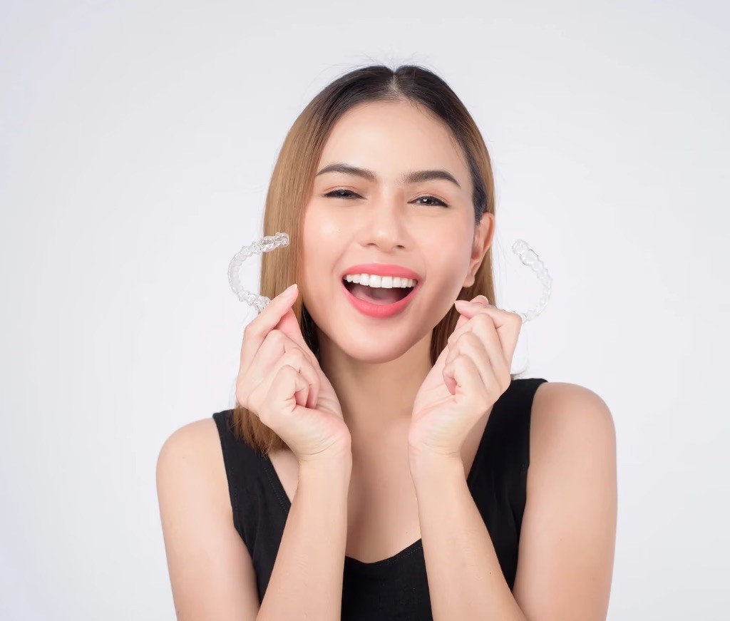 Invisalign in Dubai with a woman smiling confidently, holding her clear aligners, highlighting discreet and effective treatment.