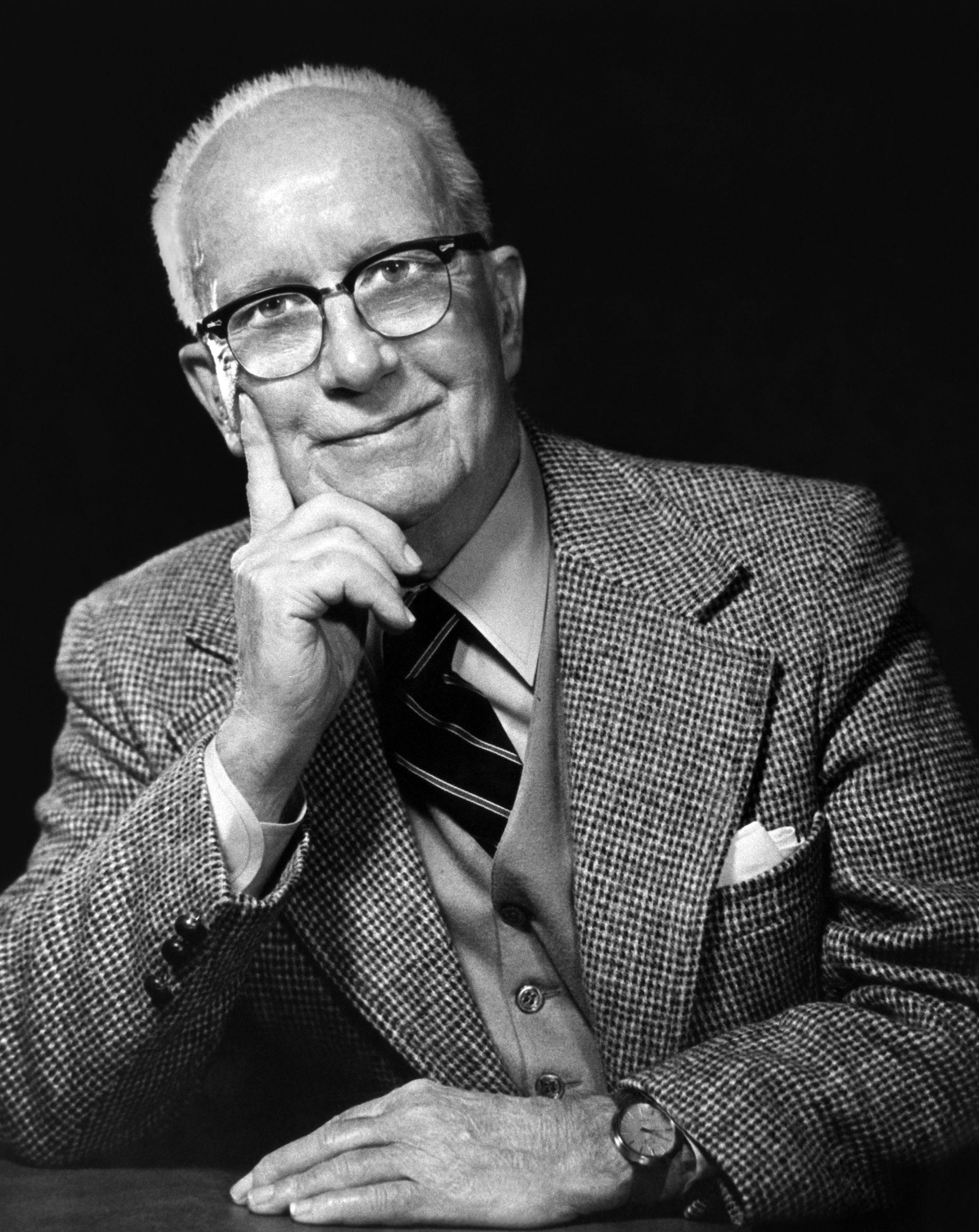 a man with his arms crossed standing in front of a desk