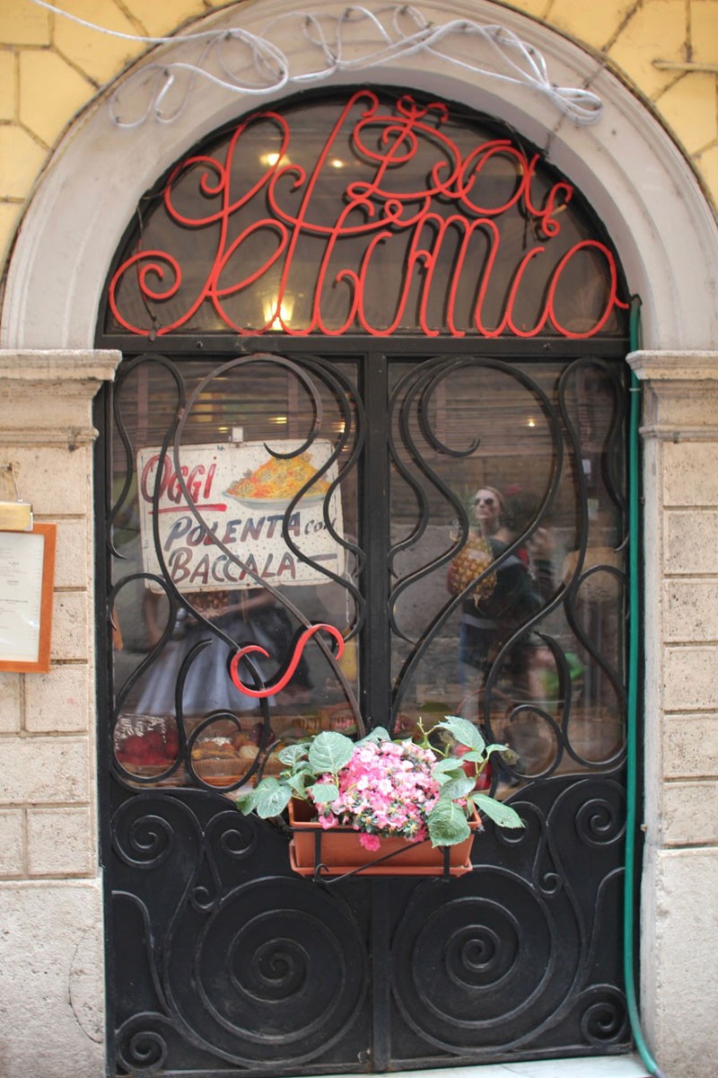 A photo of a window grill with spirals and a green and red flower in it.