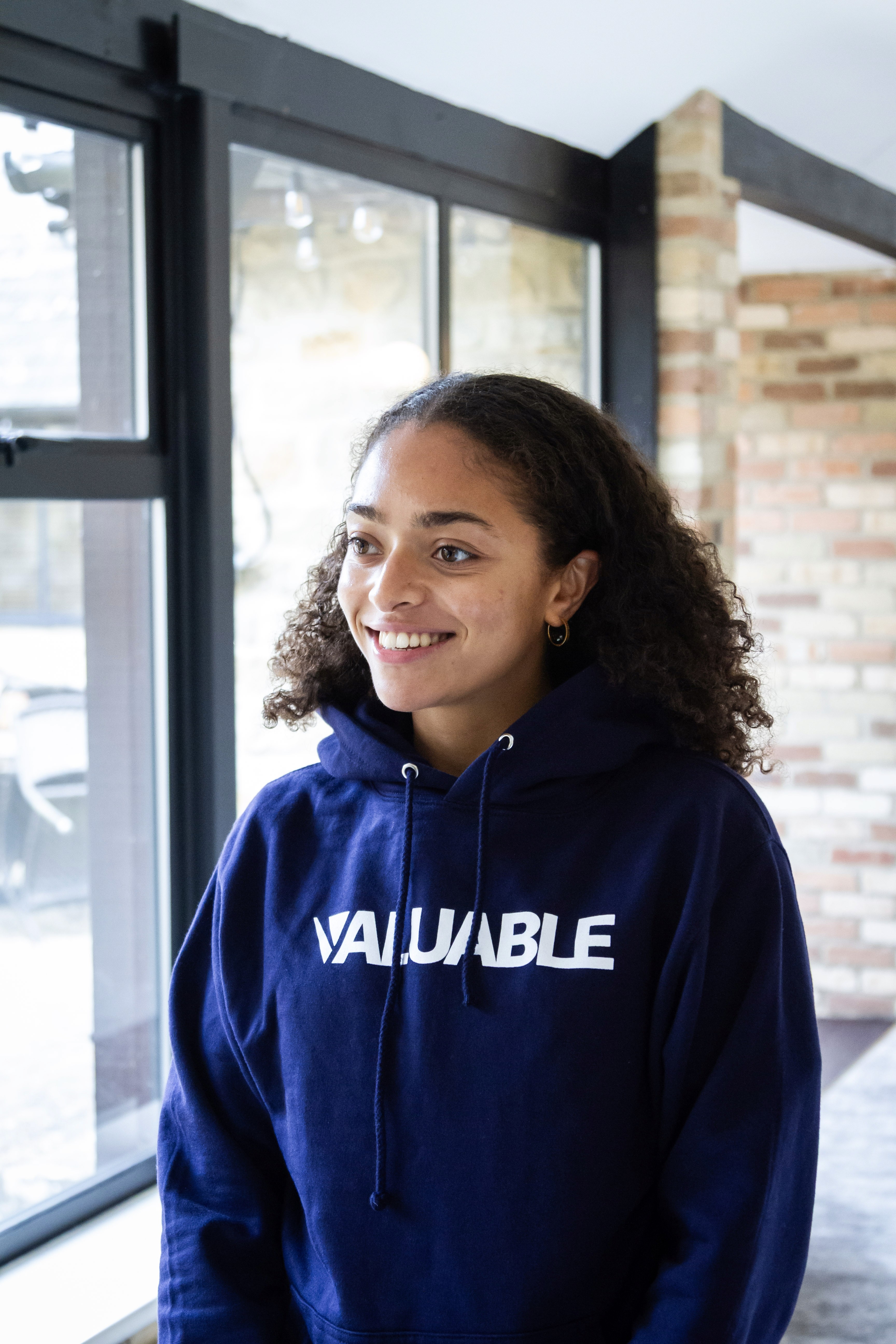 Young woman wearing a navy blue hoodie with "VALUABLE" printed in white text and smiling.