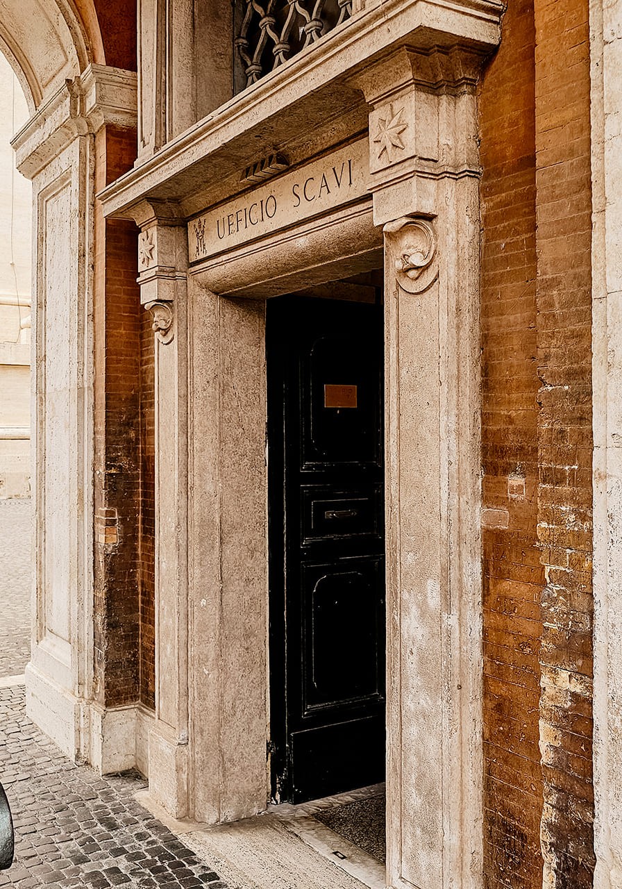 Узкий проход древнего римского некрополя под землей с кирпичной кладкой и остатками фресок при тусклом свете.