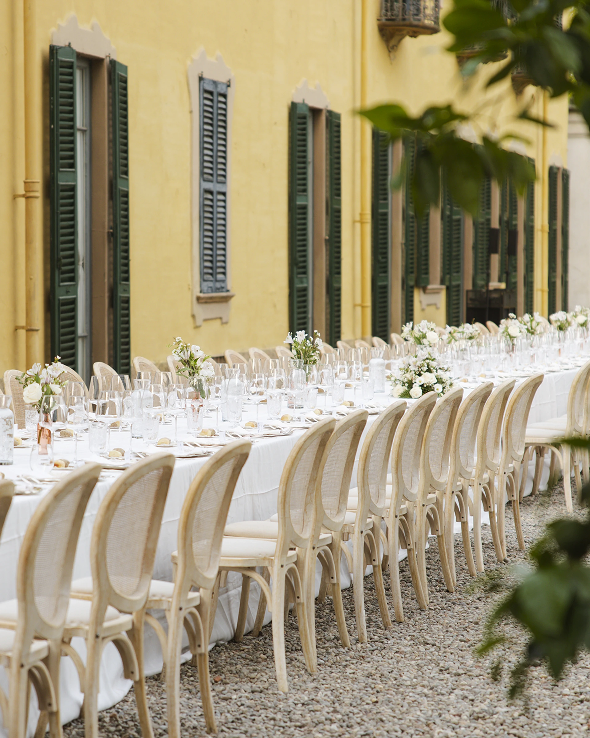 Tavolata apparecchiata davanti alla facciata gialla della villa, con composizioni di fiori bianchi