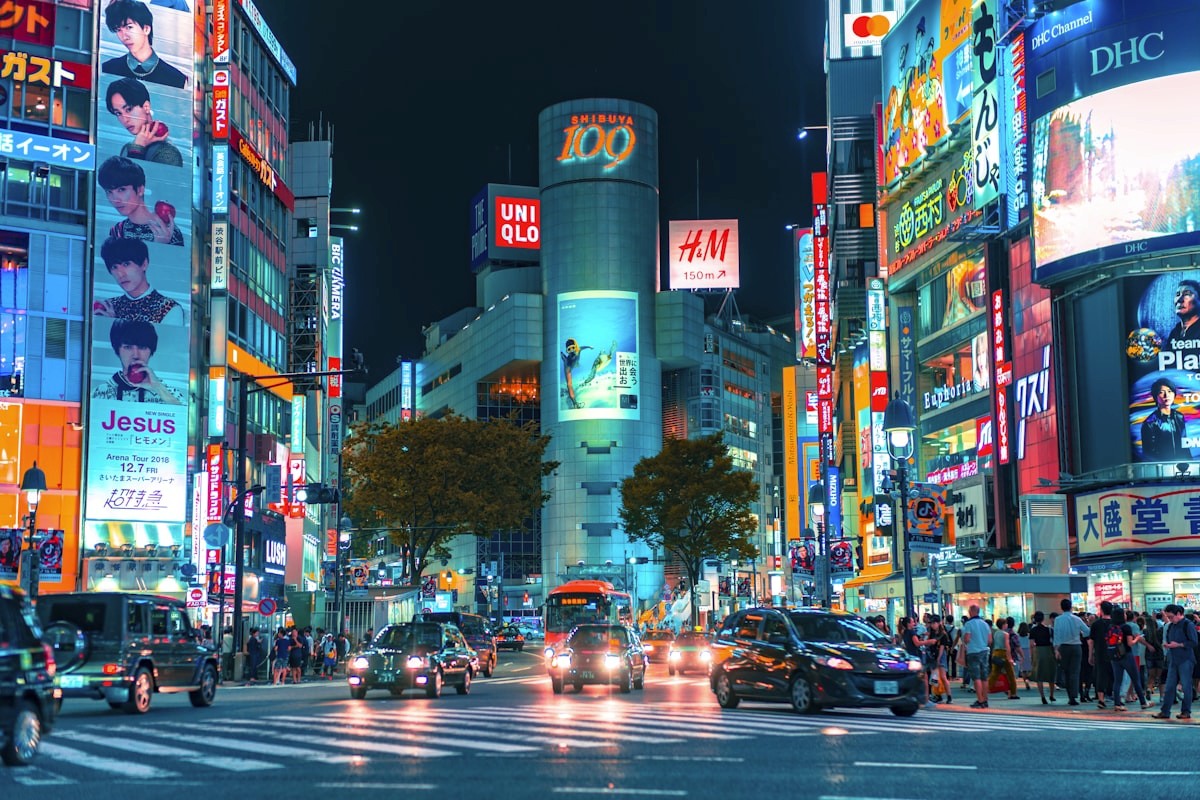 Shibuya crossing at night with neon signs reflecting off wet pavement and crowds of pedestrians