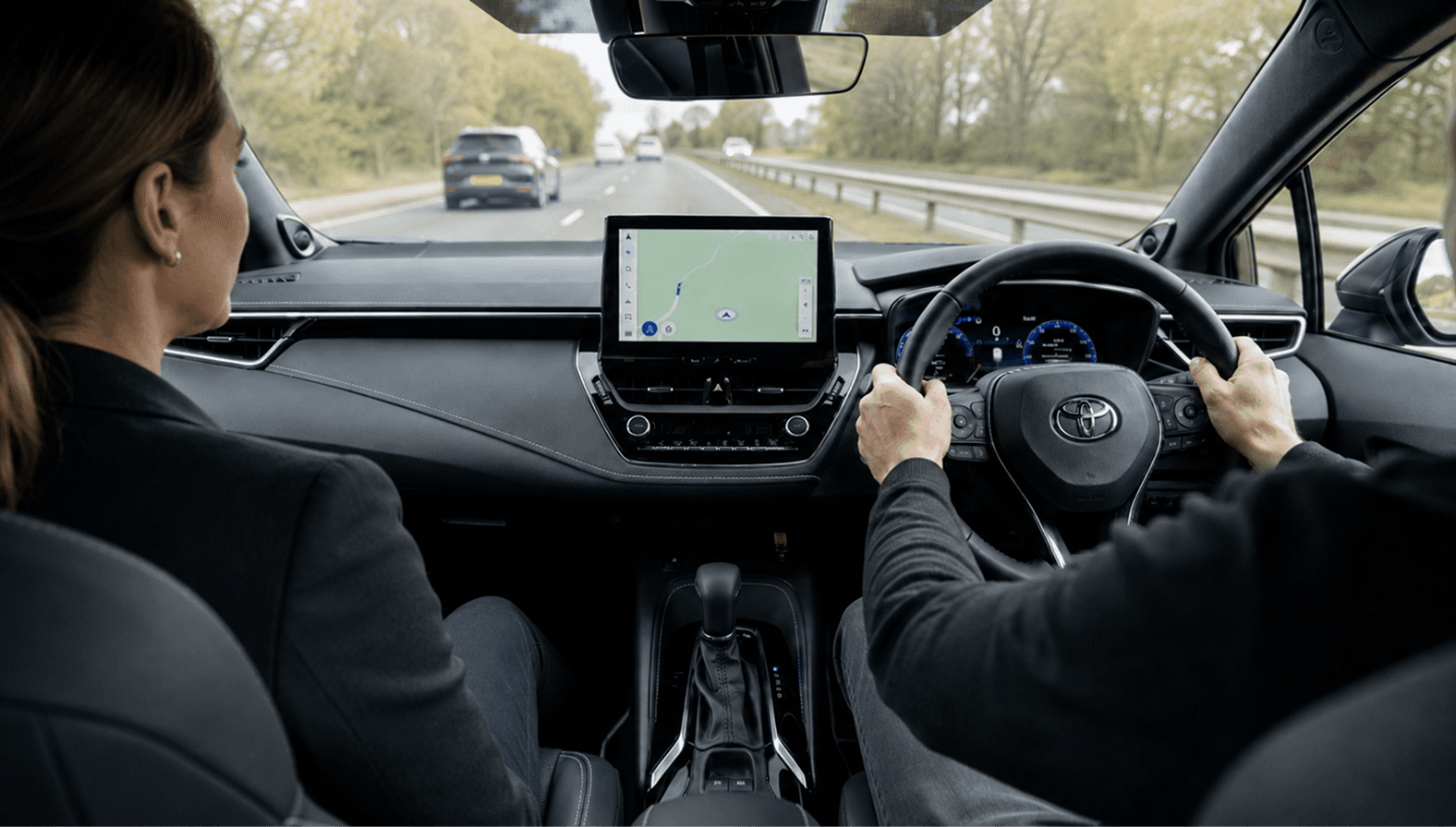 Toyota Corolla Excel interior during an automatic driving lesson, with a female instructor beside a learner driver on a daylight road.