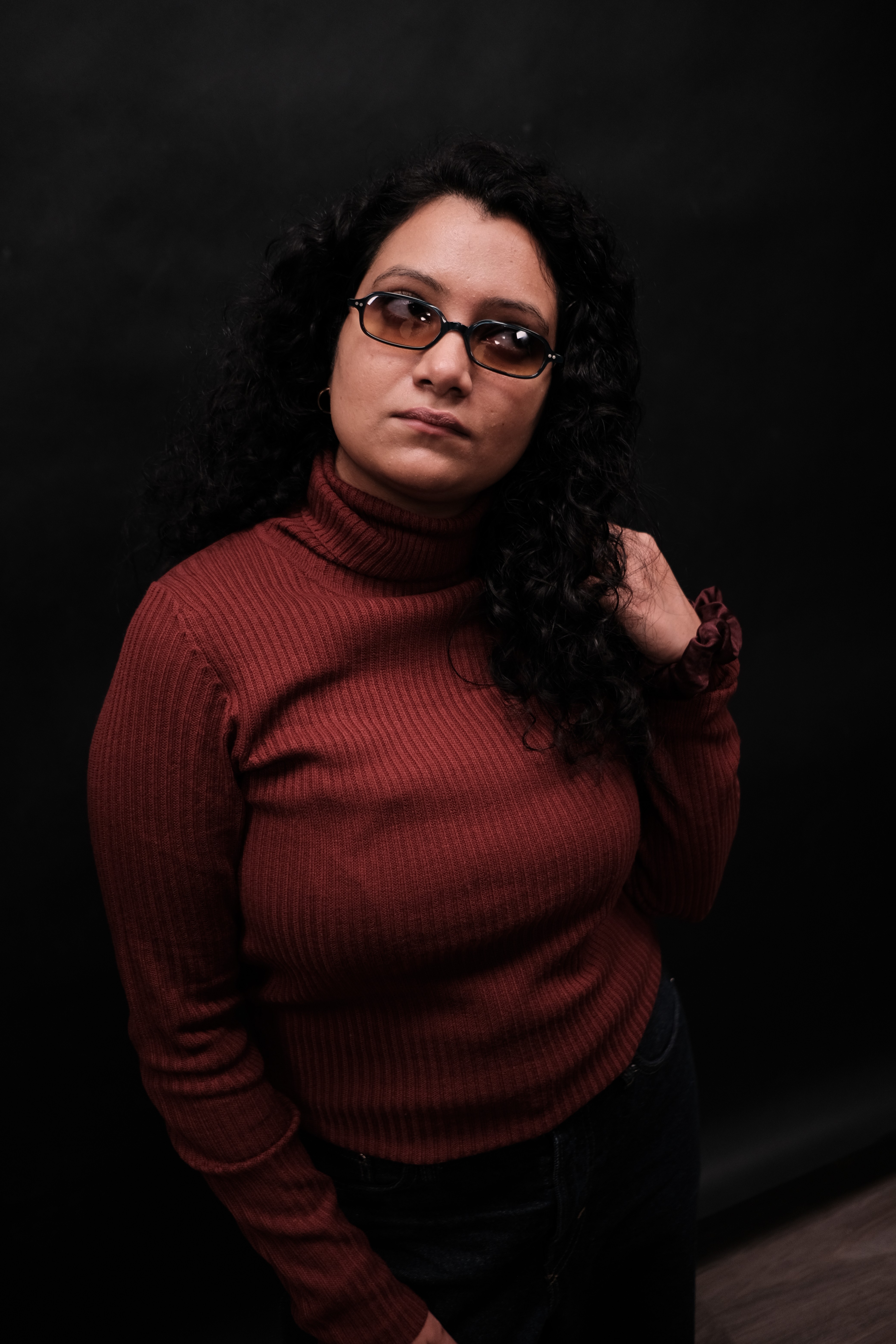 A thoughtful young person with dark hair gazes to the side, captured in soft black and white lighting.