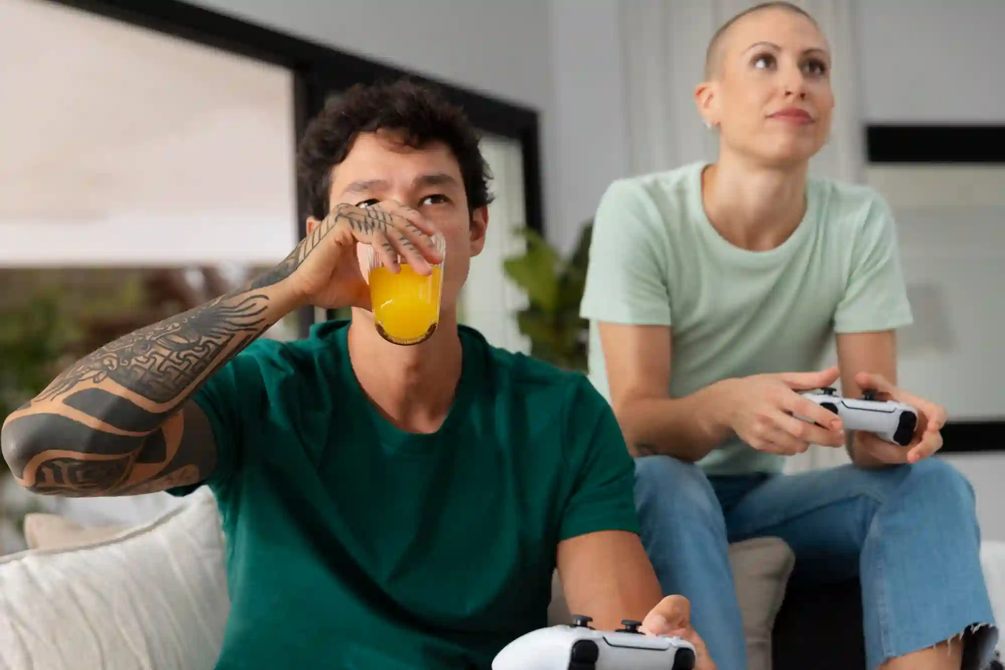 A couple playing video games and drinking juice on a couch.