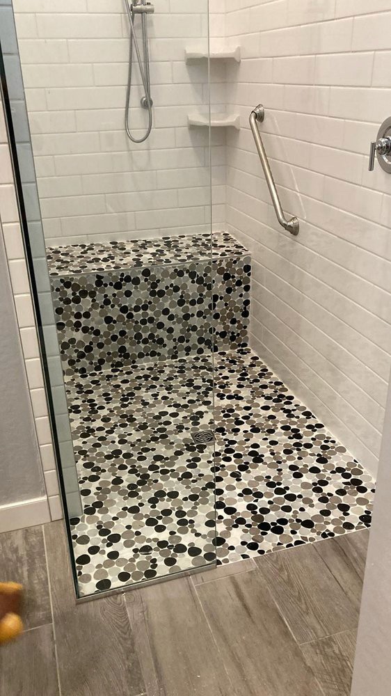 Modern shower with white subway tile walls, a built-in bench and shower floor fully tiled with multi-toned circular pebble mosaics in black, grey, and white.
