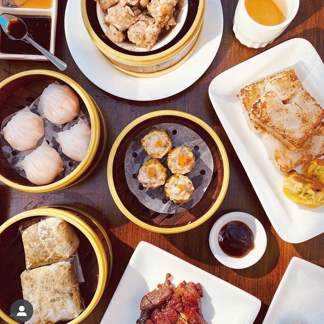 A vibrant spread of traditional dim sum dishes at Jing Fong, including BBQ pork buns, rice noodle rolls, shumai, and egg tarts, served on elegant white plates in their Chinatown location.